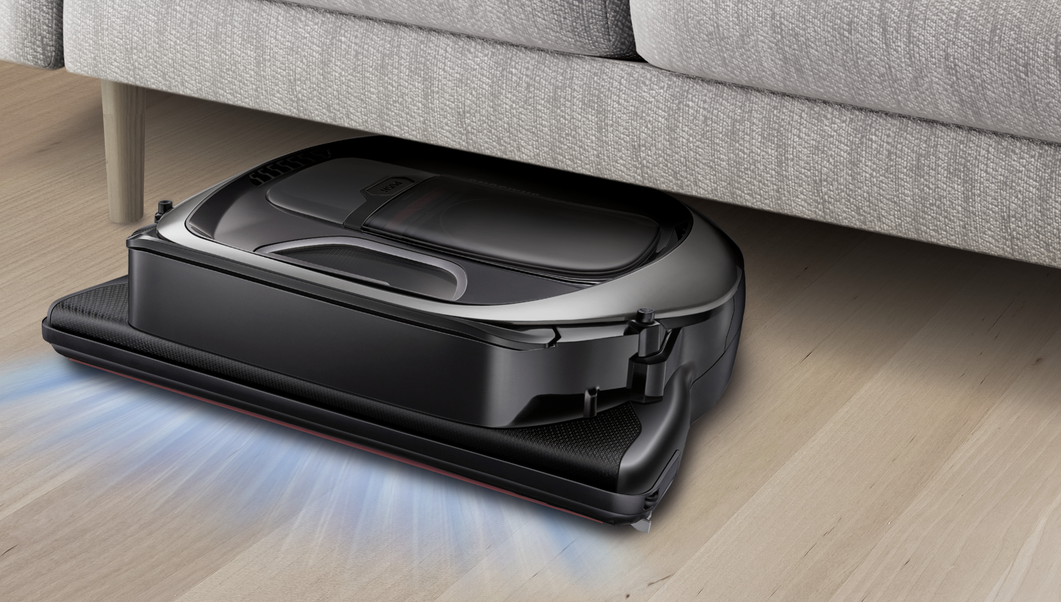 Roboter-Staubsauger unter einem Sofa, der einen Holzboden reinigt.