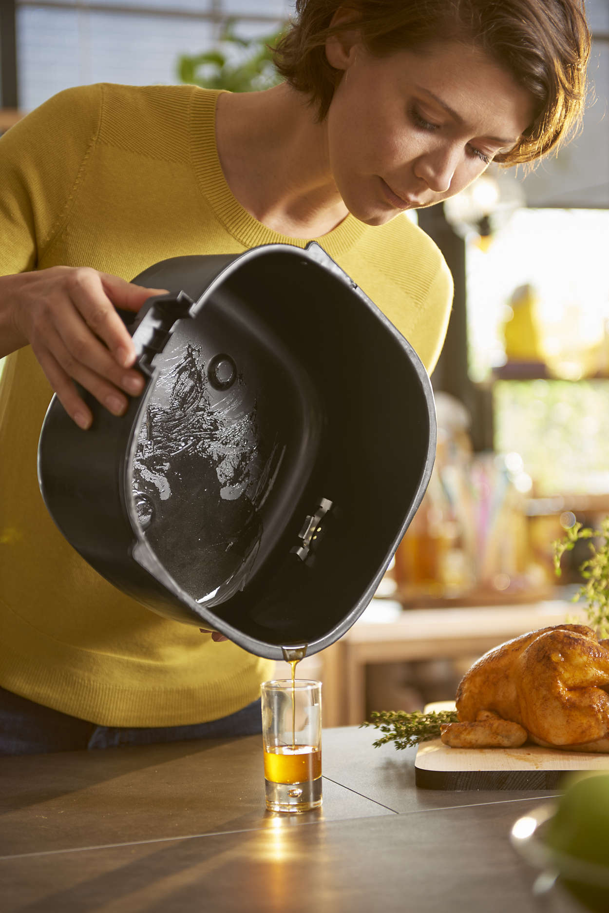 Vrouw die olie uit een zwarte airfryer in een glas giet.