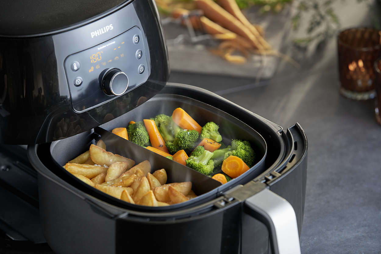 Friteuse à air avec légumes et frites. Le couvercle est ouvert. Carottes et brocolis. Frites dans l'autre section.