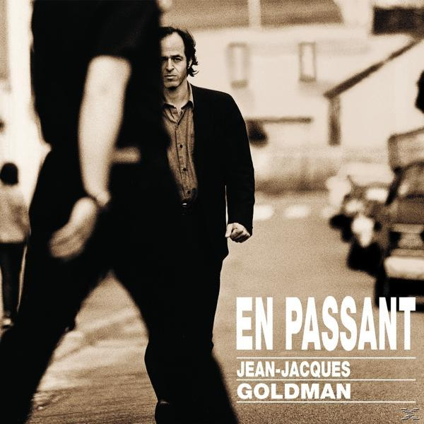 Man loopt, deels bedekt, op straat. Albumhoes met tekst 'En Passant' en Jean-Jacques Goldman.