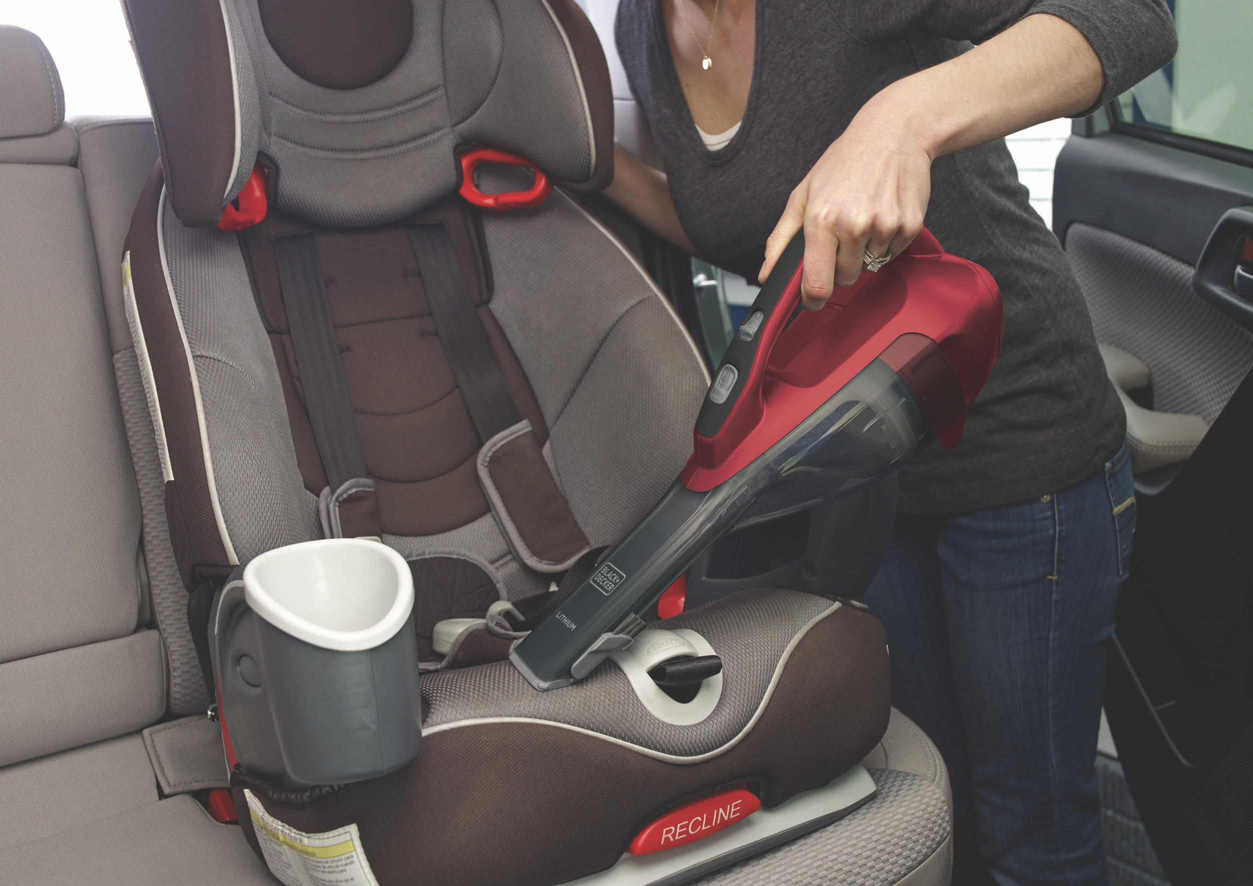 Eine Person saugt einen Autositz mit einem rot-schwarzen Handstaubsauger ab. Auto Interieur.