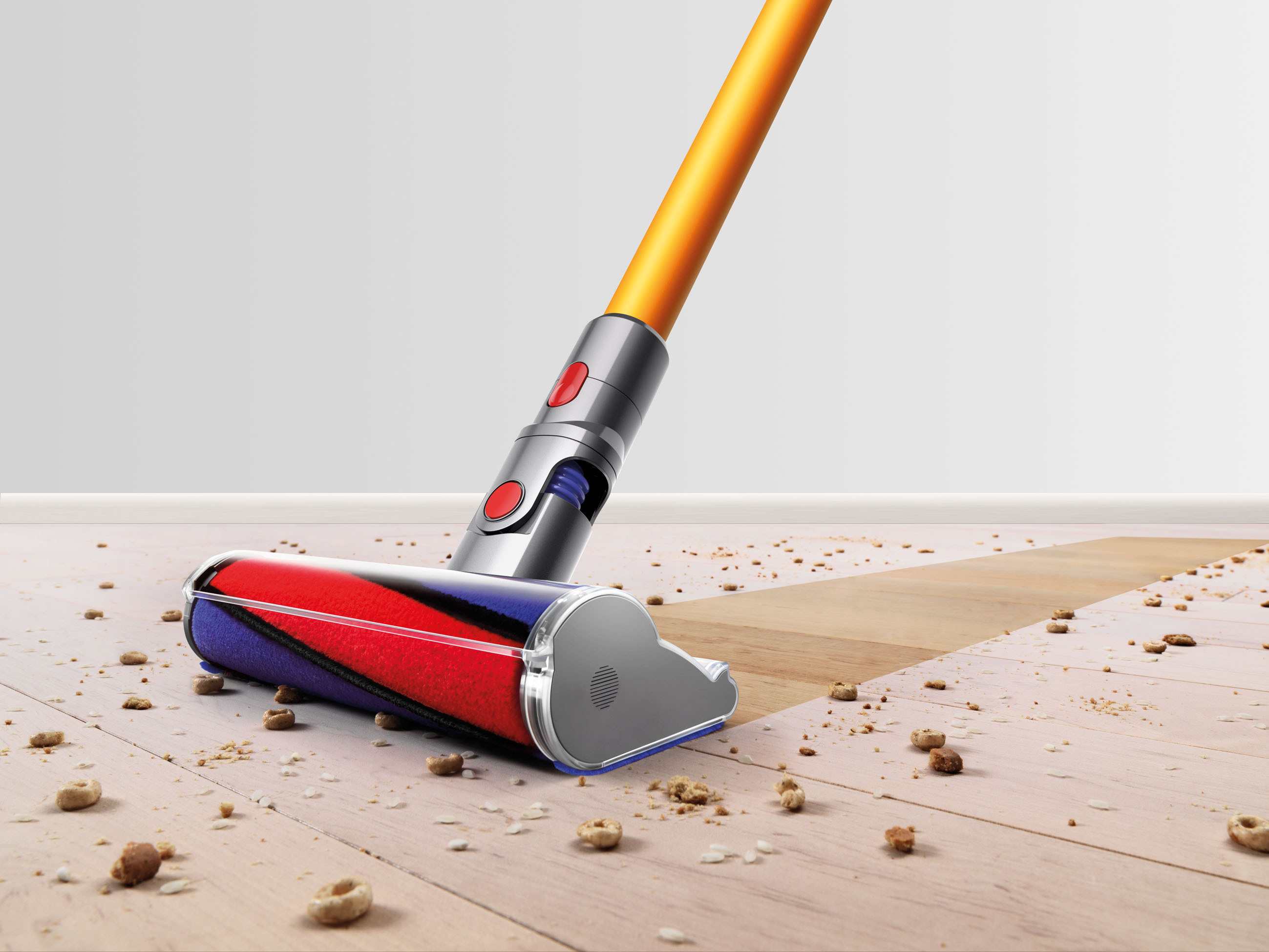 Ein Staubsauger mit einer rot-blauen Bürste reinigt Krümel auf einem Holzboden. Orangenes Rohr, grauer Körper.