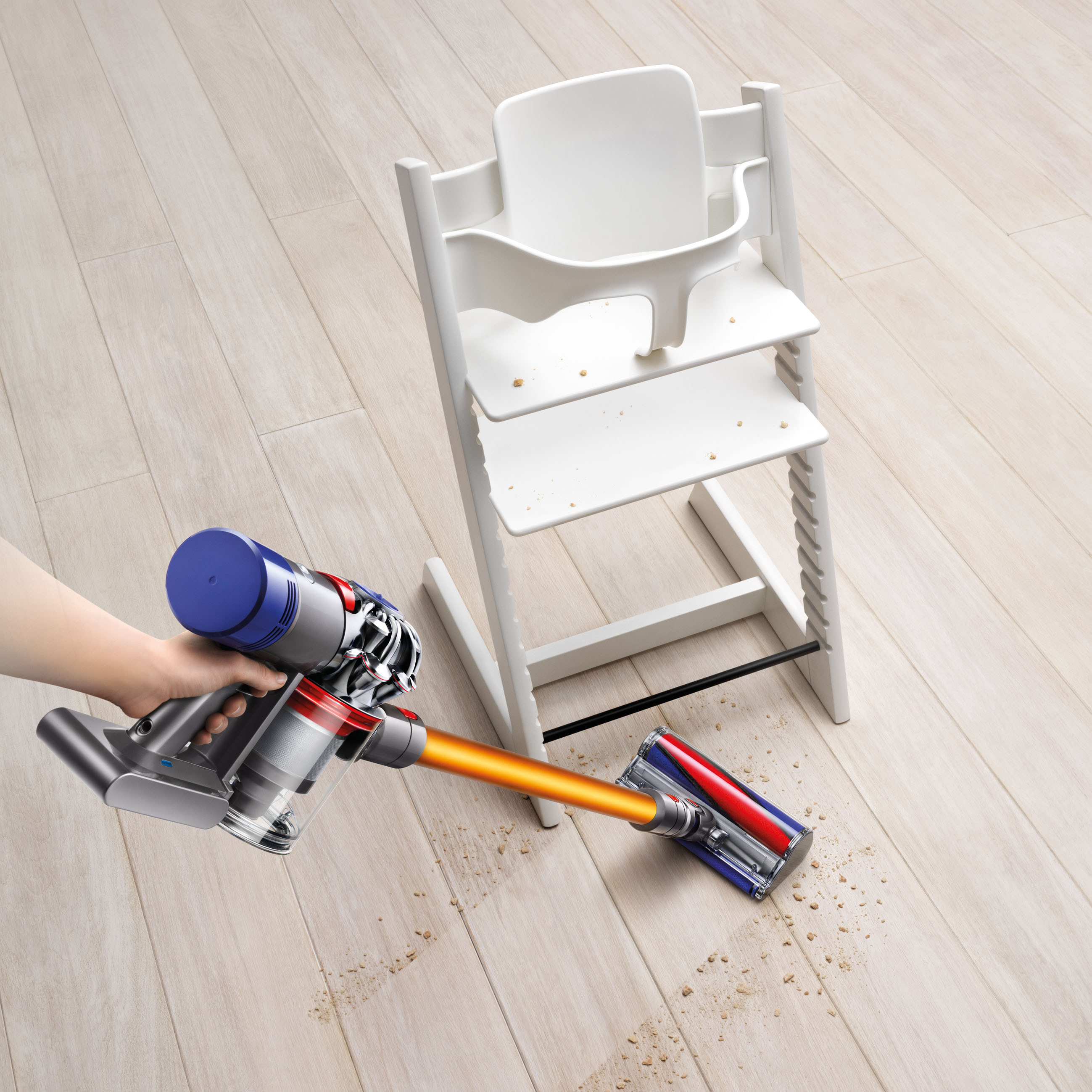 Eine Person saugt einen Holzboden in der Nähe eines Hochstuhls mit einem Dyson-Staubsauger.