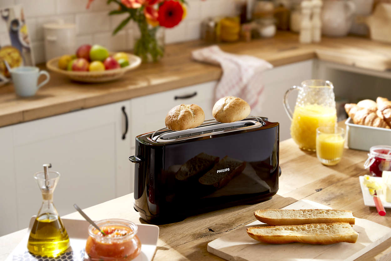Black toaster with two toasted bread slices and a table setting with food items.