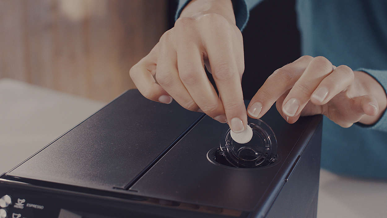Person inserting a coffee pod into a black espresso machine. White surface.
