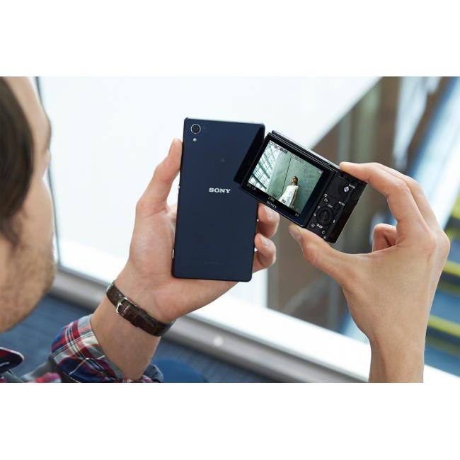 Une personne tenant un téléphone noir et un appareil photo plus petit, deux écrans.