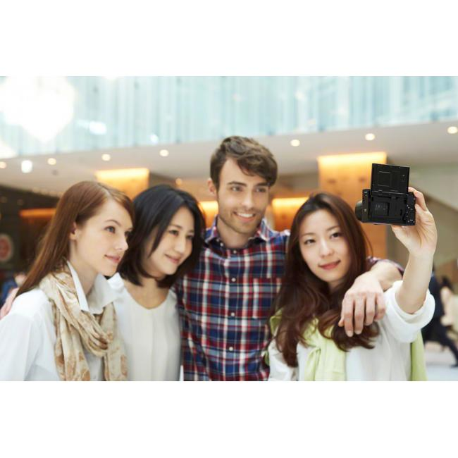 Quatre personnes prennent un selfie. L'une tient un appareil photo. Elles sont dans un couloir lumineux.