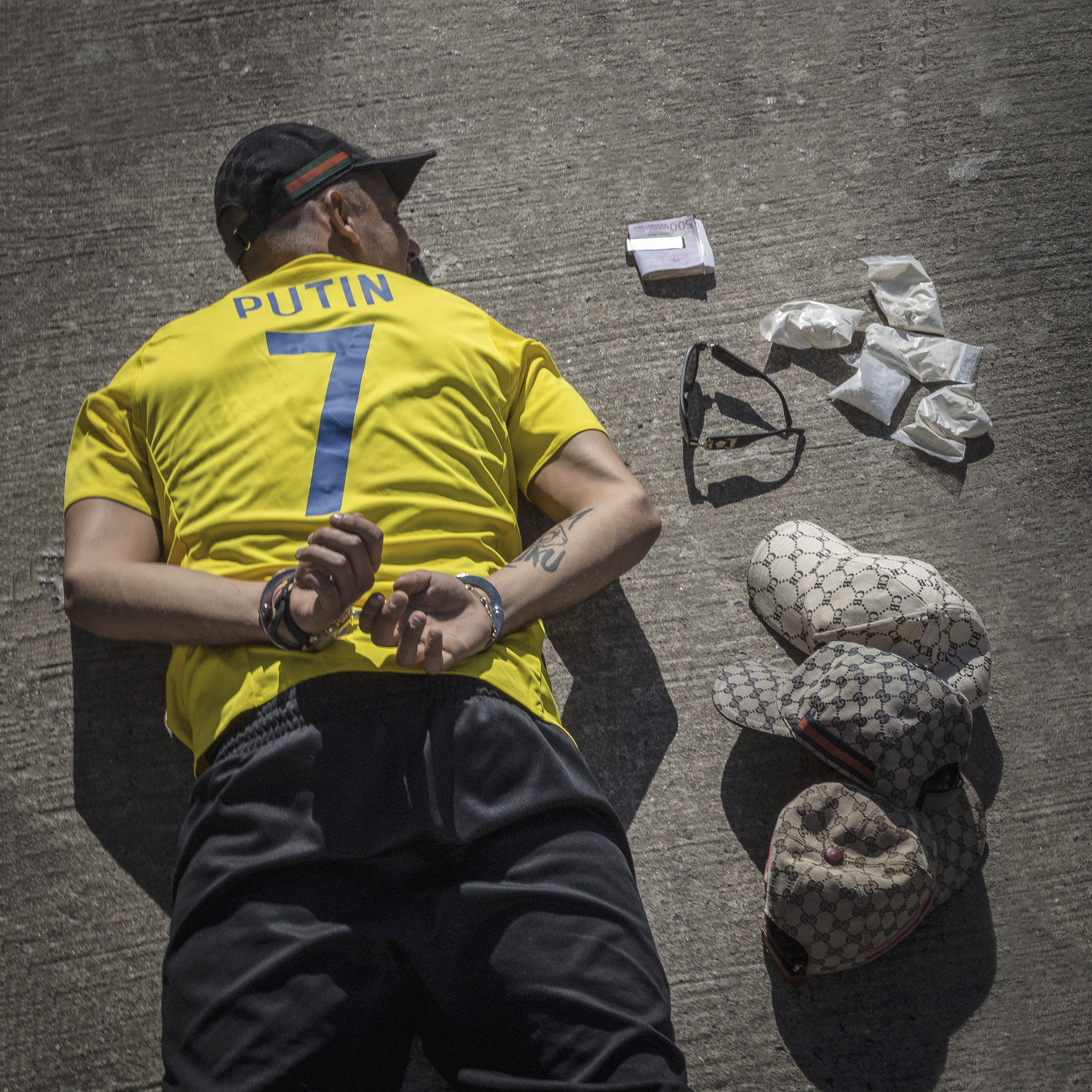 Ein Mann in gelbem Trikot mit "PUTIN" und der Nummer 7 liegt gefesselt mit Drogen am Boden.