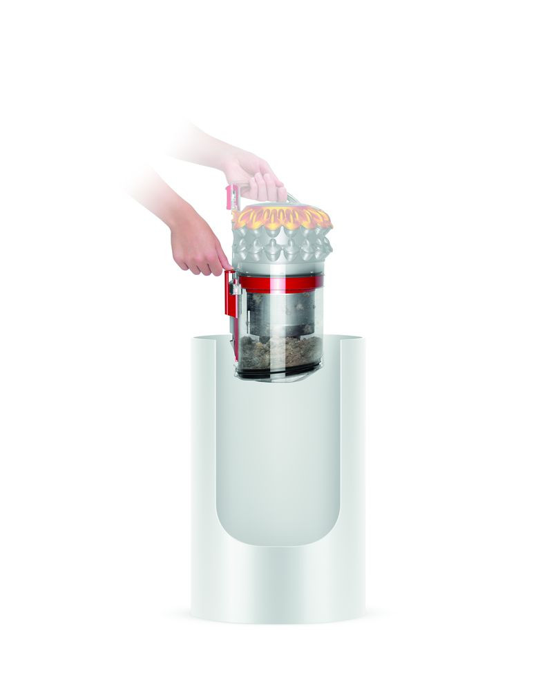 Une main vidant un réservoir d'aspirateur rouge et blanc dans une poubelle blanche.