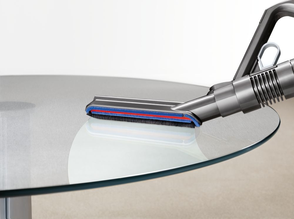 Aspirateur nettoyant une table en verre. La tête de brosse est visible. La table est ronde.