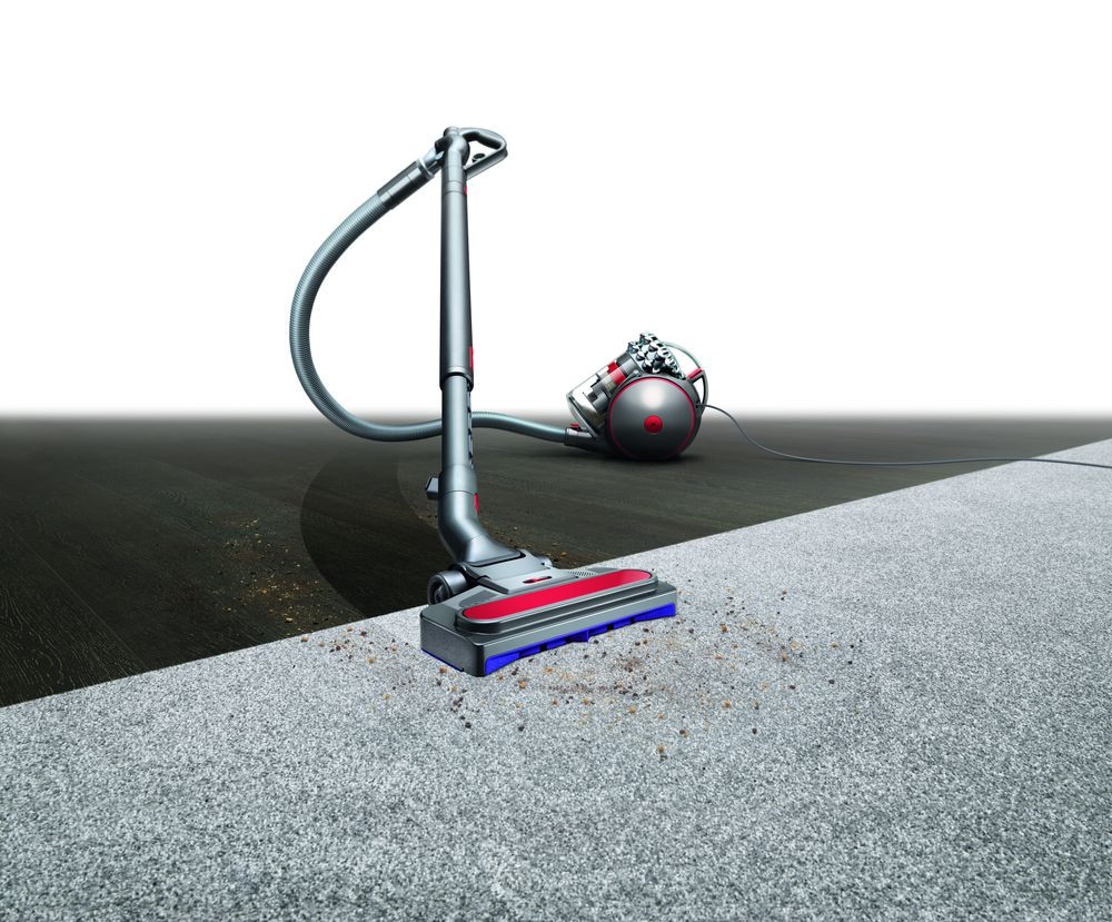 Vacuum cleaner on carpet, cleaning. Gray body, red accents. Dark wood floor and light carpet.