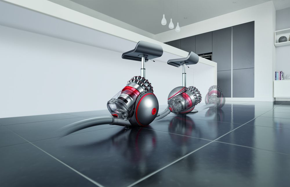 Dyson vacuum cleaners in a kitchen. Red and silver design. Grey floor tiles. White background.