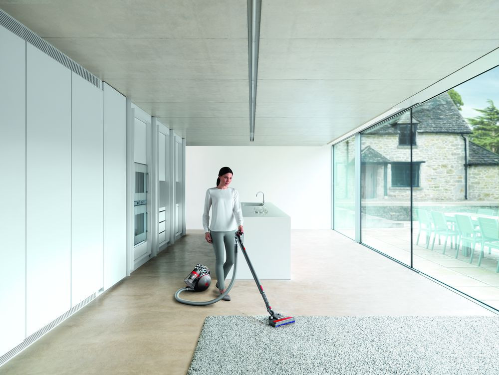 Woman vacuuming a white floor. Red and gray vacuum cleaner.