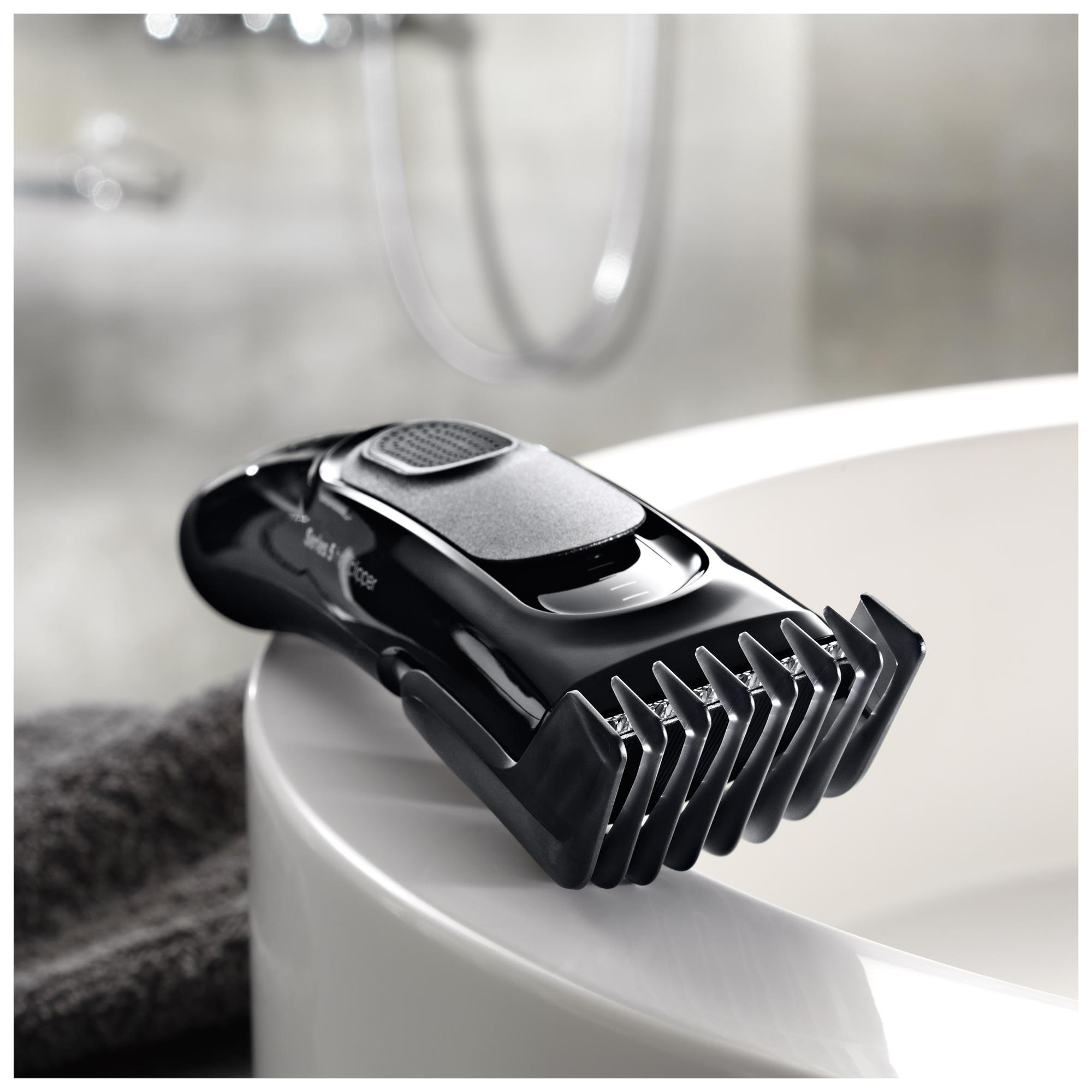 Schwarzer Haarschneider auf einem weißen Waschbecken. Schwarzer Trimmer, graues Handtuch. Badezimmerumgebung.