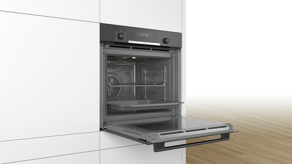 Ein offener Einbau-Backofen in einer weißen Küche, mit geöffneter Tür.