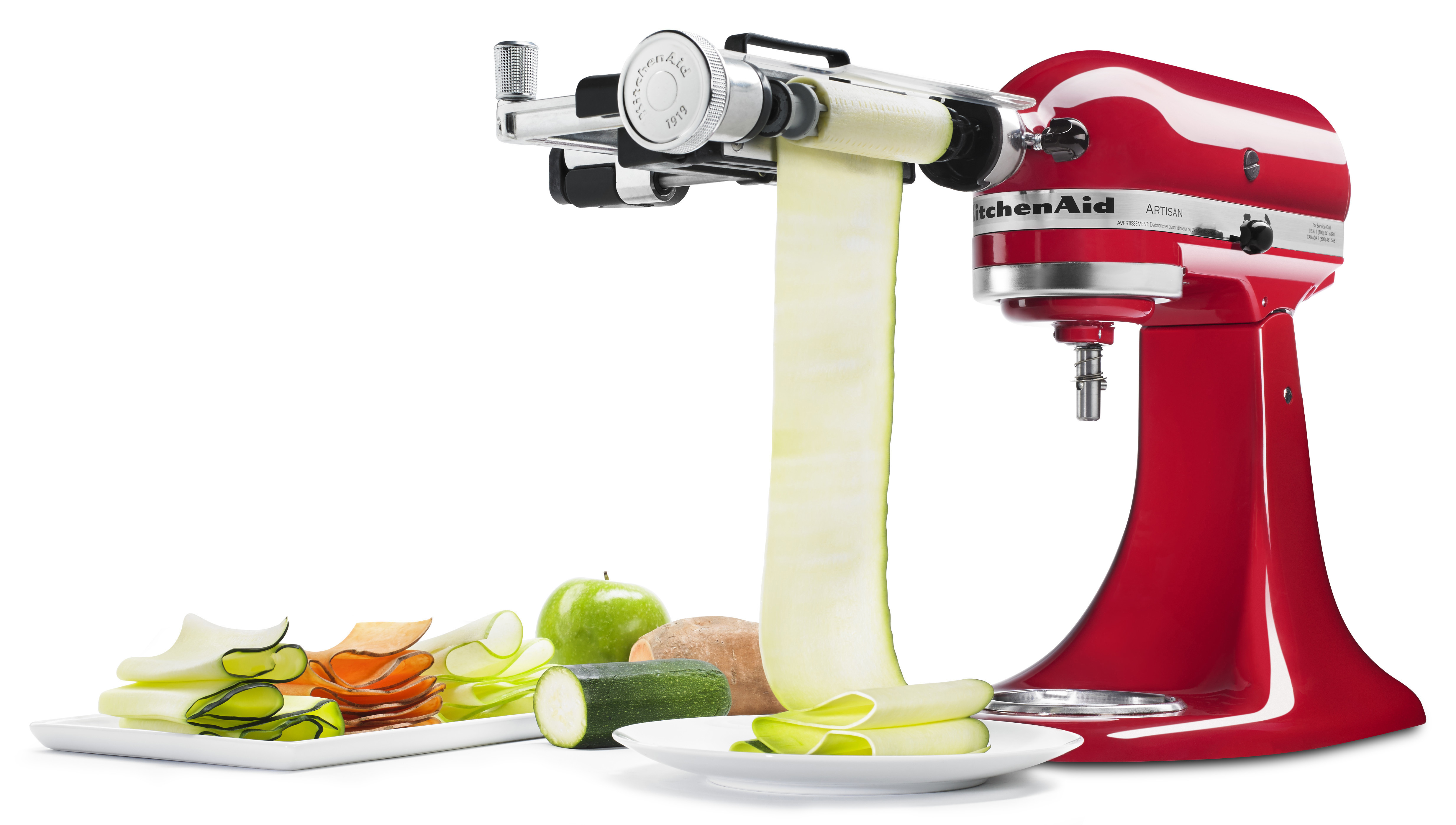 Ein roter KitchenAid-Mixer mit einem Spiralschneider-Aufsatz, der Gemüsebänder auf einen Teller erzeugt.