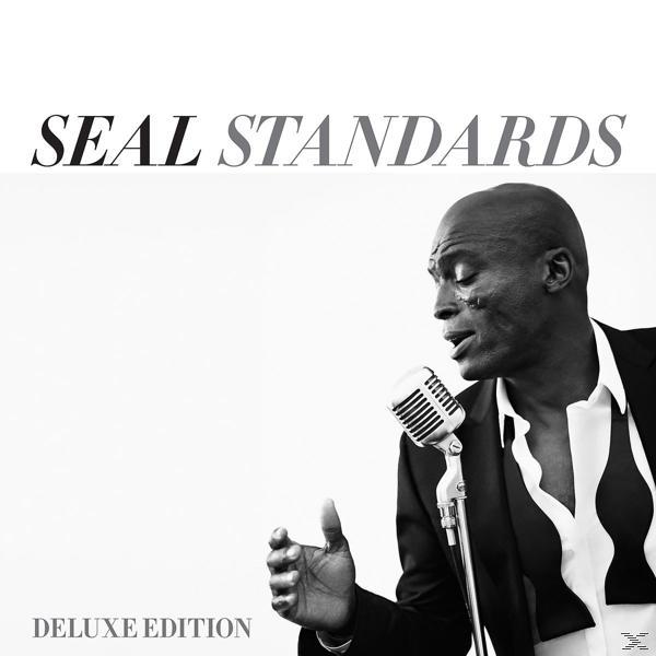 Seal zingt in een microfoon, zwart pak, albumtekst: Seal Standards Deluxe Edition.