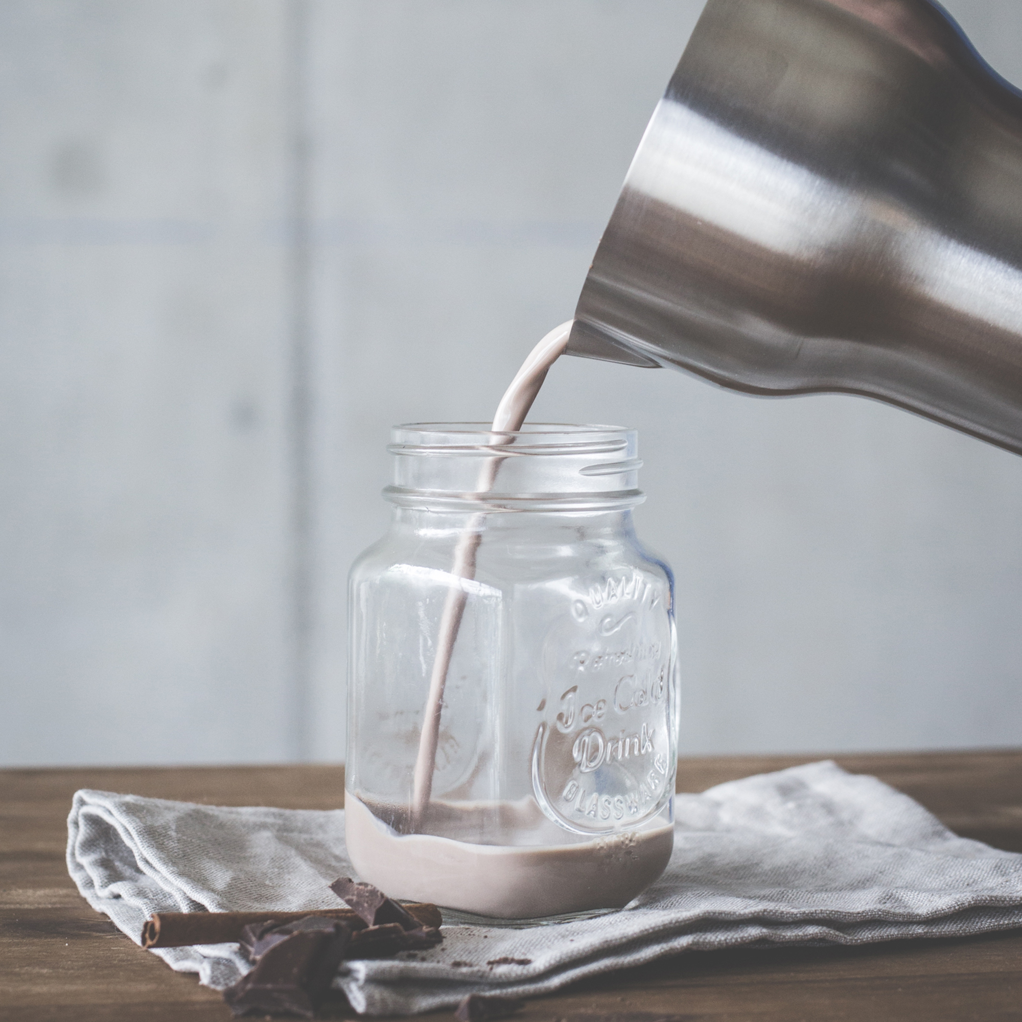 Schokoladendrink, der in ein Glasgefäß auf einem Holztisch gegossen wird.