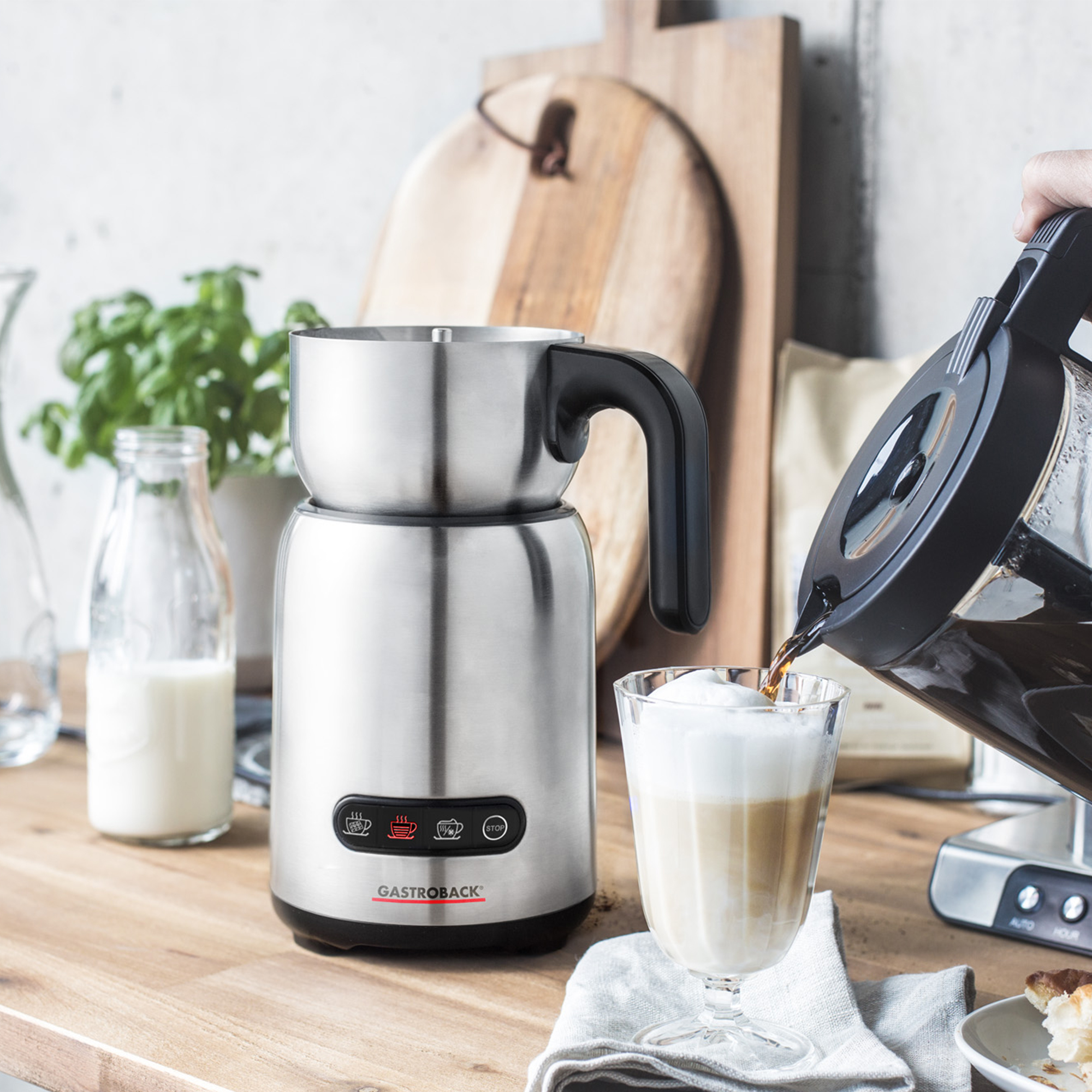 Kaffee wird in ein Glas mit Milchschaum gegossen, neben einem Milchaufschäumer.