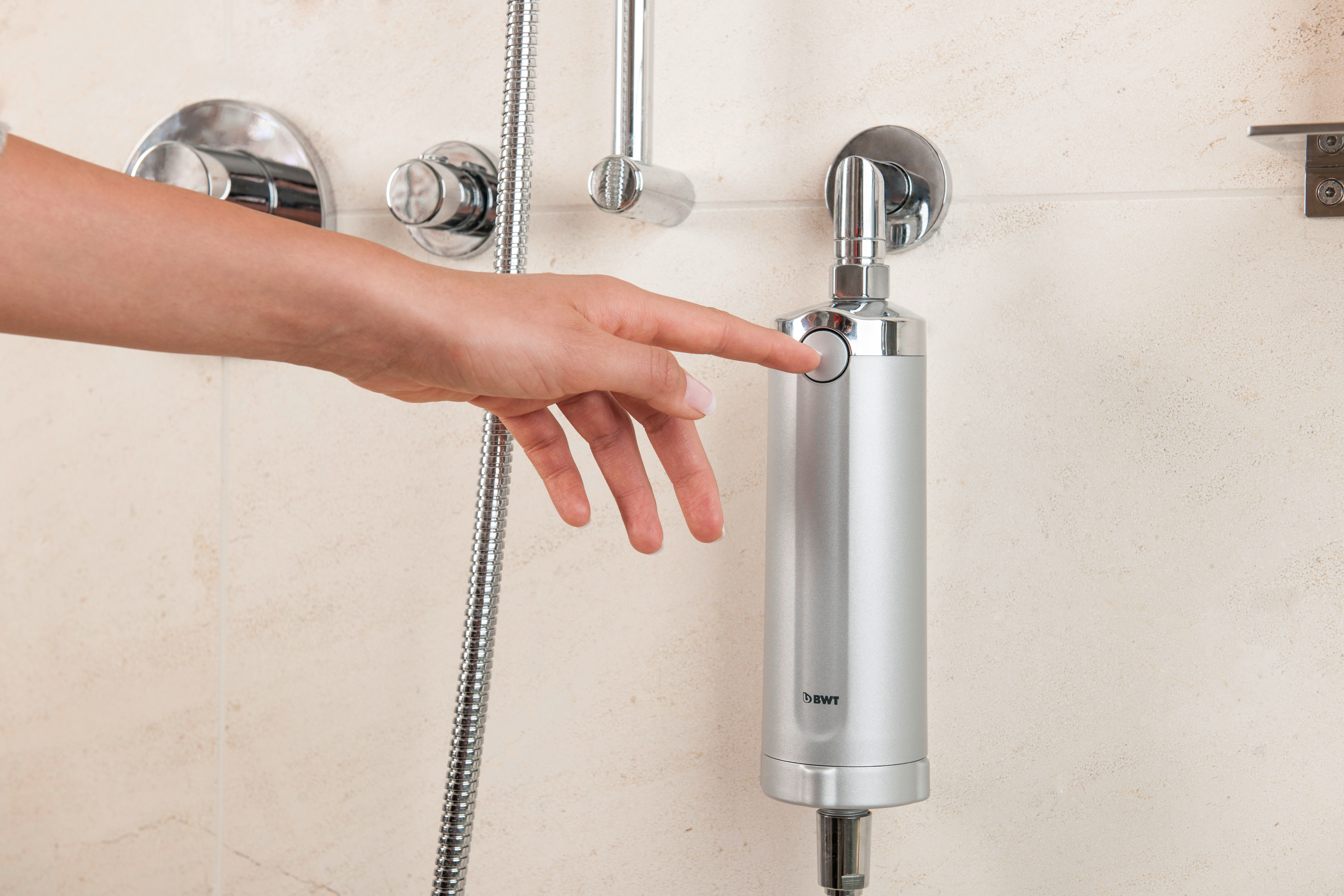 Eine Hand drückt einen Knopf an einem silbernen BWT-Wasserfilter, der an einem Duschkopf befestigt ist.