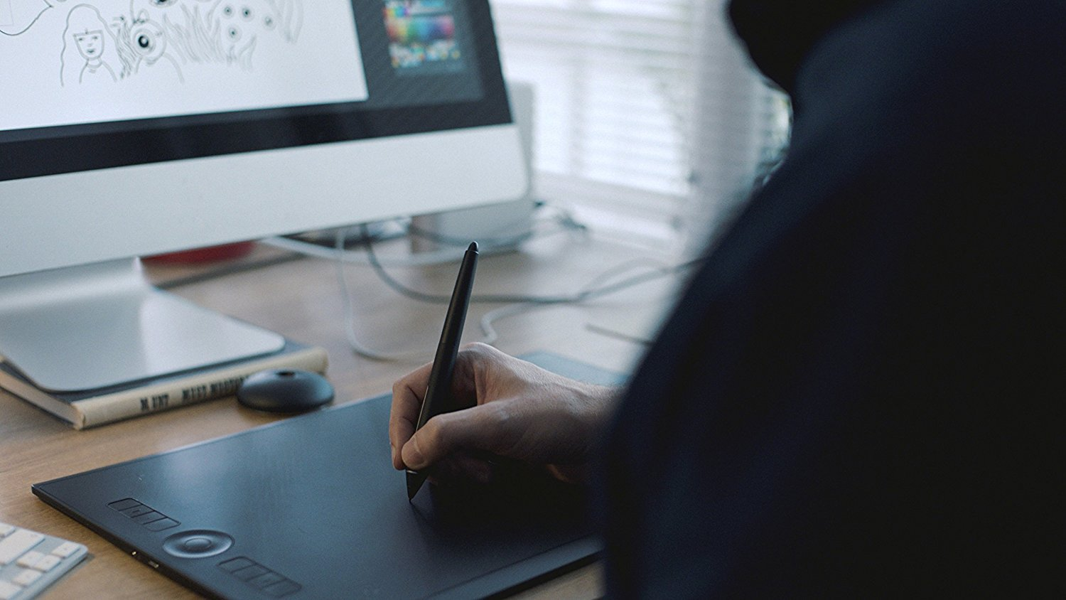 Eine Person zeichnet mit einem Stift auf einem Grafiktablett vor einem Computerbildschirm.