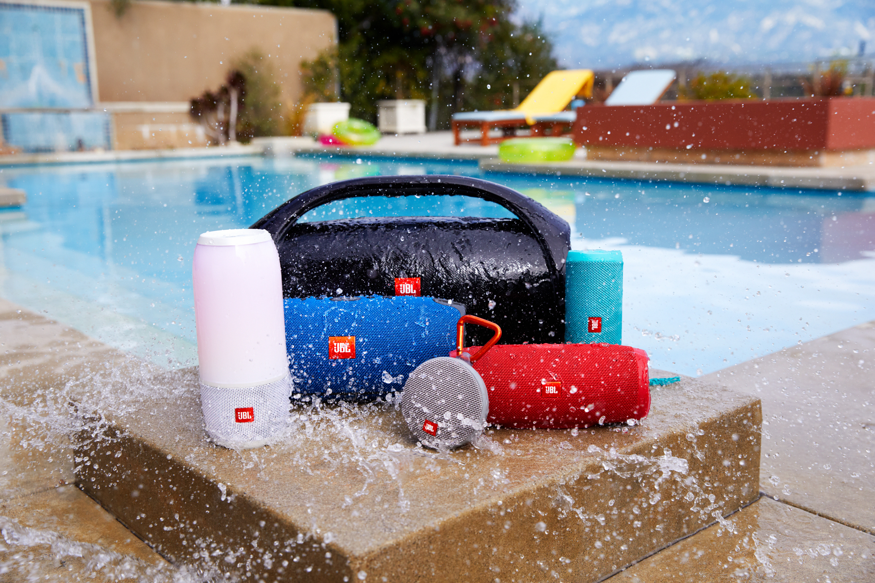 JBL-Lautsprecher an einem Pool. Rosa, blaue und schwarze Lautsprecher mit Wasserspritzern.