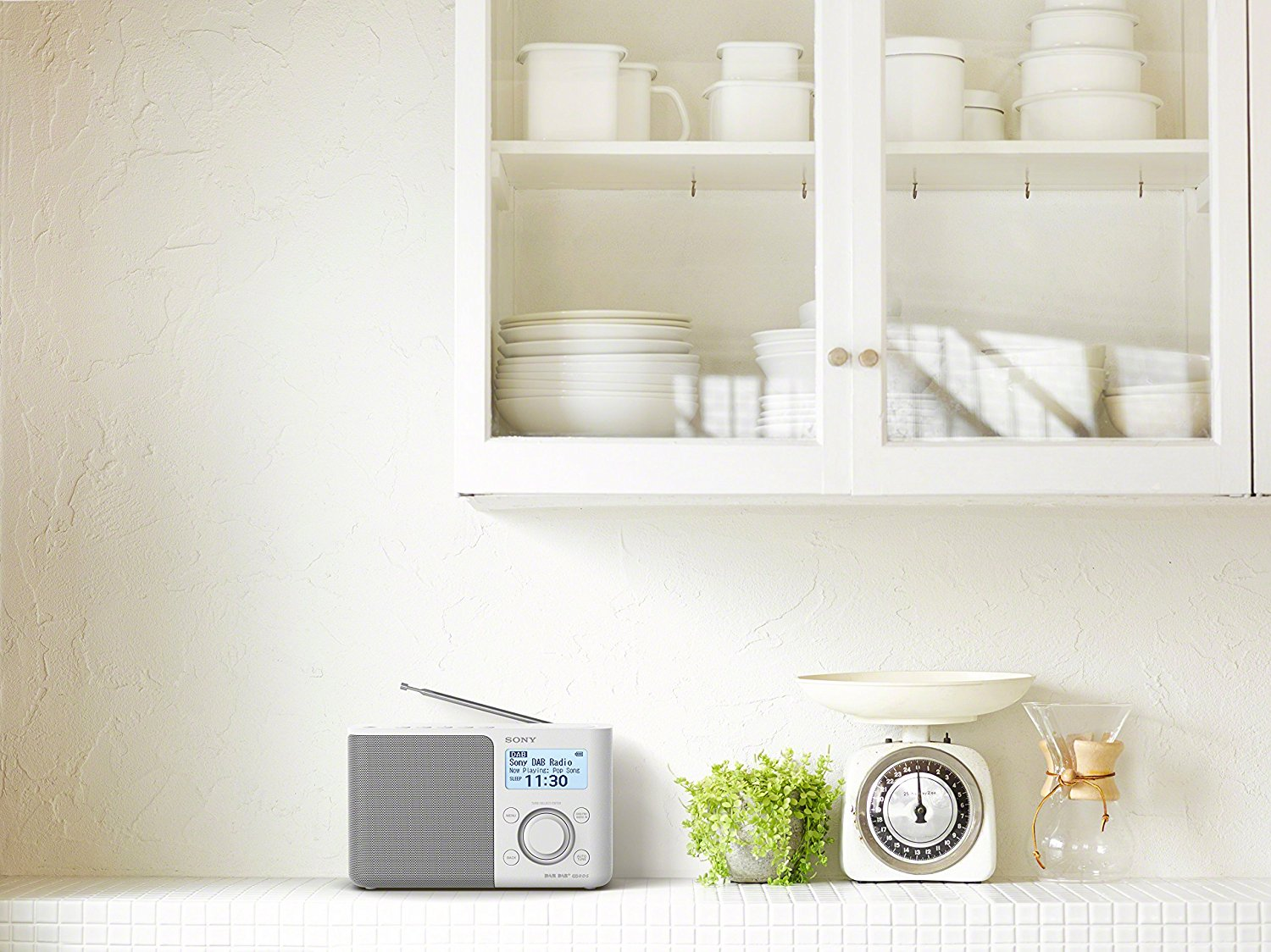 Keuken met radio, weegschaal en planten. Witte kasten op de achtergrond.