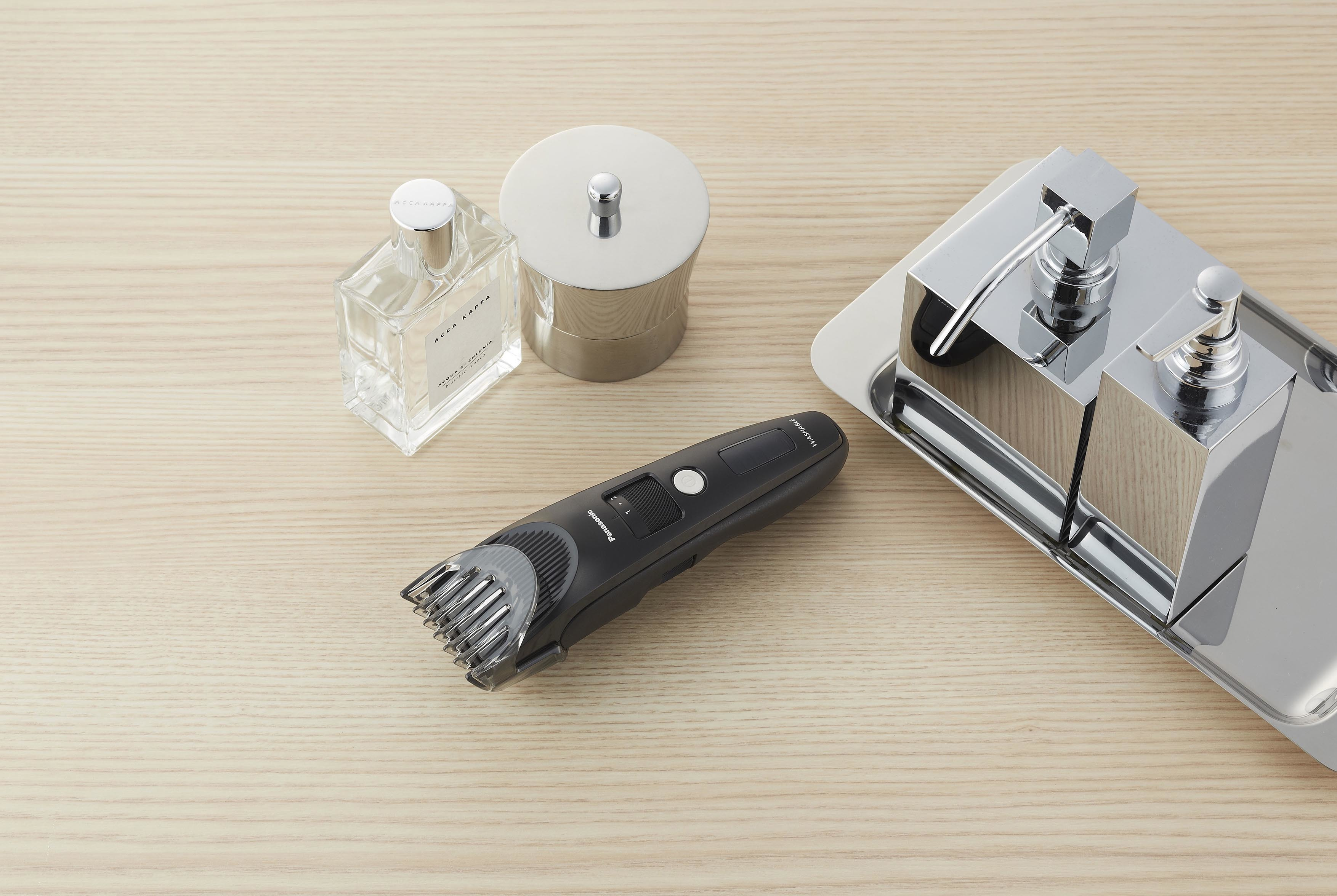 Aménagement de salle de bain : parfum, récipient en métal, tondeuse, distributeur de savon sur bois clair.