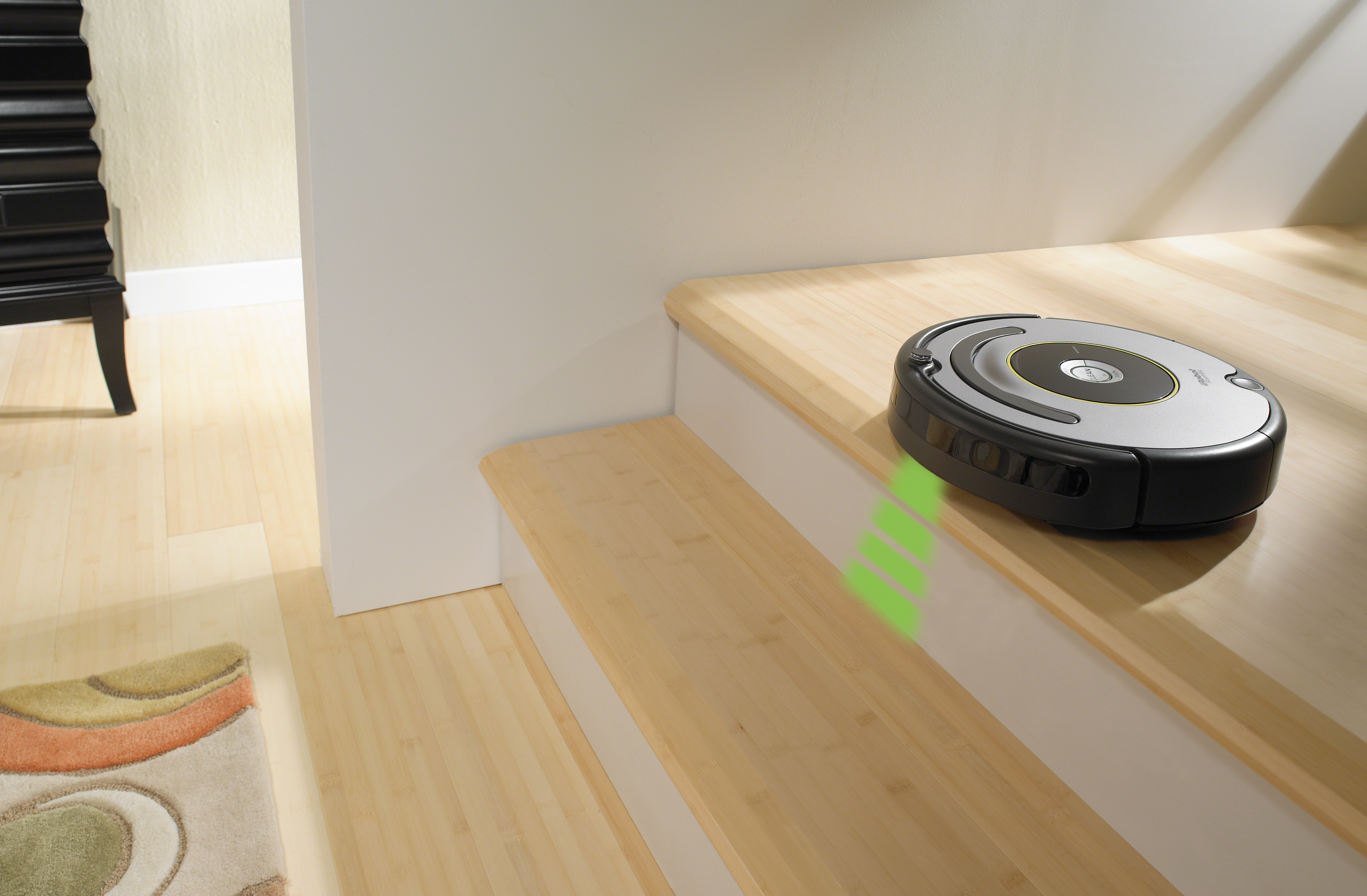 Ein Roboter-Staubsauger auf Holztreppen. Der Roboter ist schwarz und grau, mit einem grünen Licht, das die Treppe hinunter scheint.
