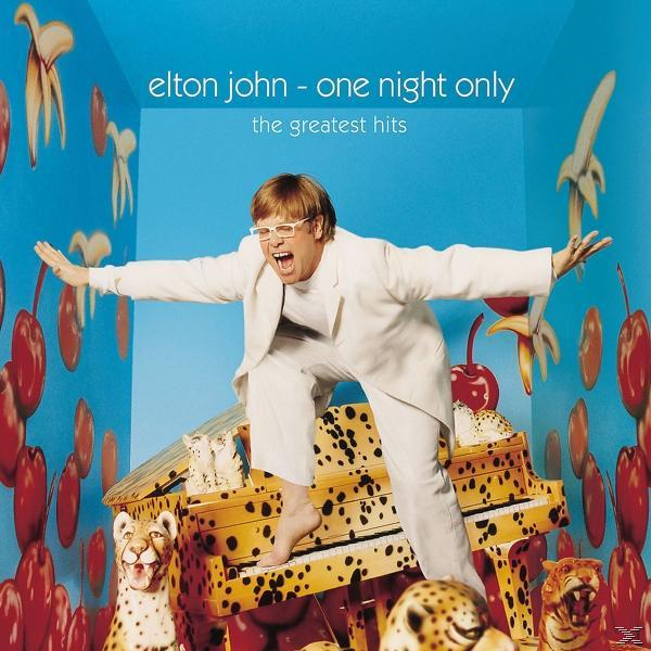 Elton John auf einem Klavier, in weißer Kleidung, Arme ausgestreckt, blauer Hintergrund.