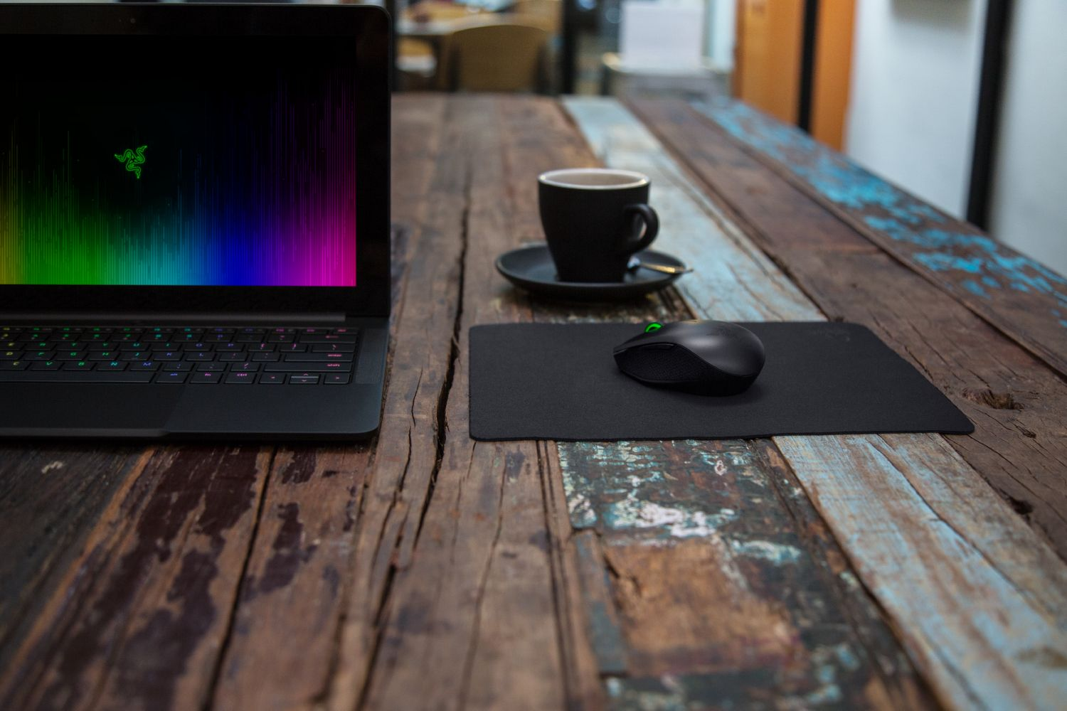 Ordinateur portable, souris noire et tasse sur une table en bois rustique.