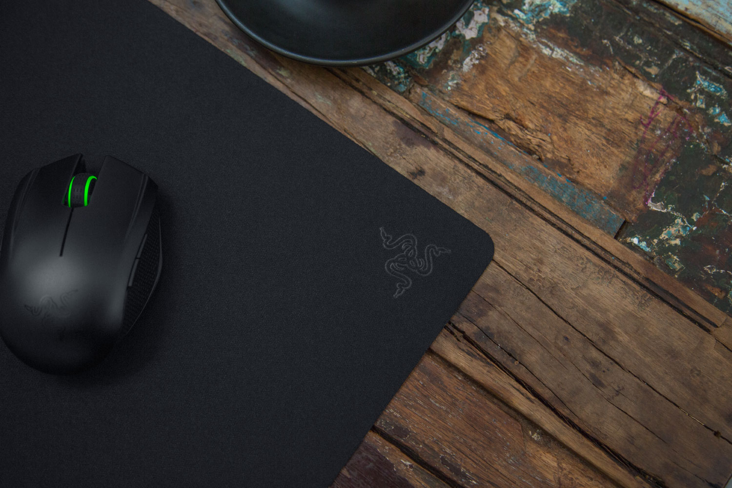 Souris et tapis de souris Razer noirs sur une table en bois. La souris a des accents verts, et le logo Razer est visible.