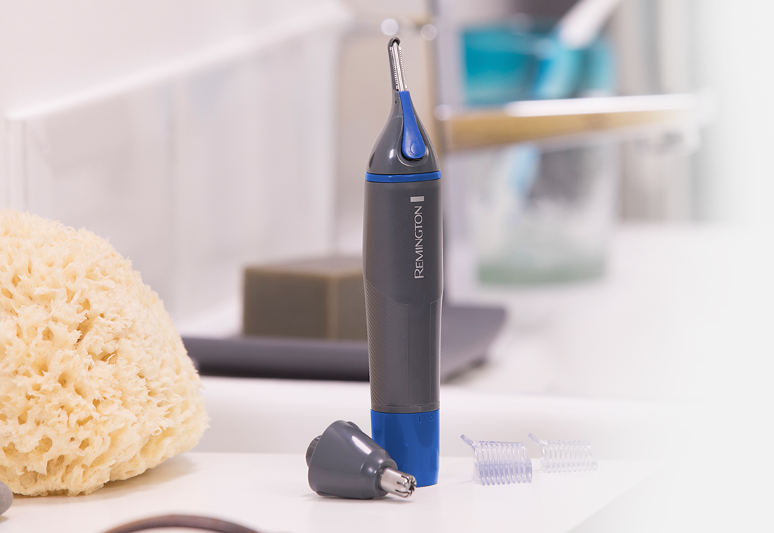 A gray and blue Remington nose and ear trimmer.  Accessories are next to it and a sponge.