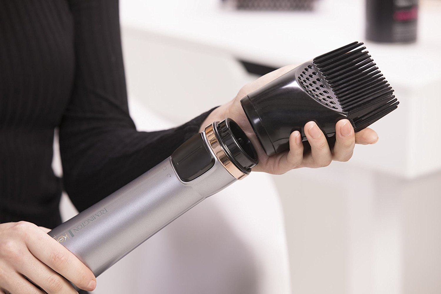 A woman attaching a black comb attachment to a silver and black hair dryer.