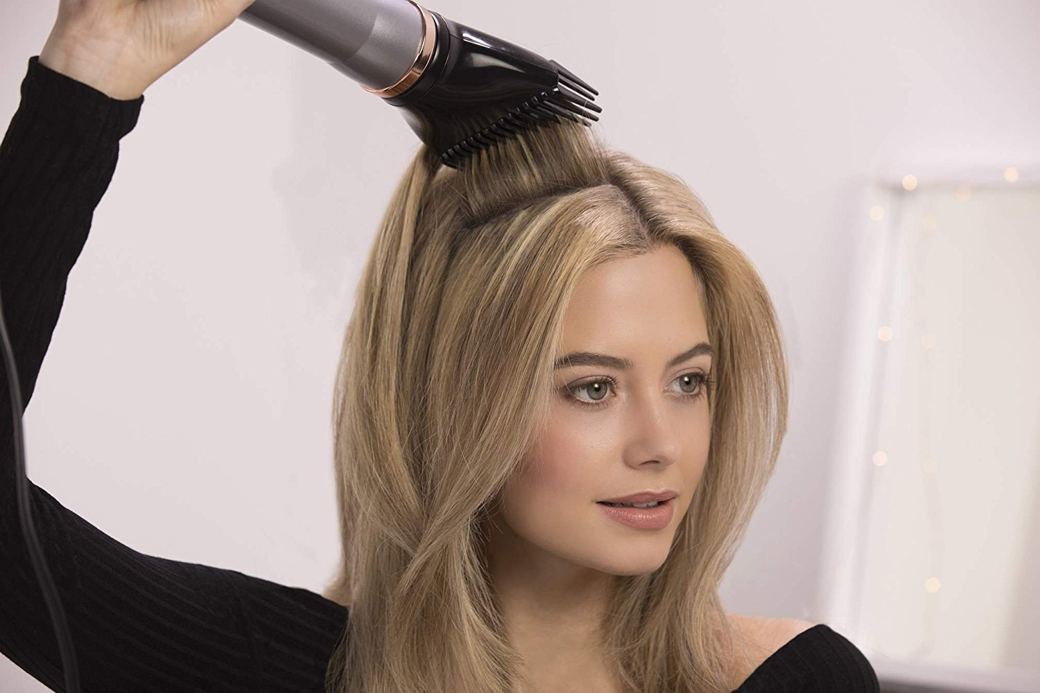 A woman blow-drying her blonde hair with a black hair dryer.
