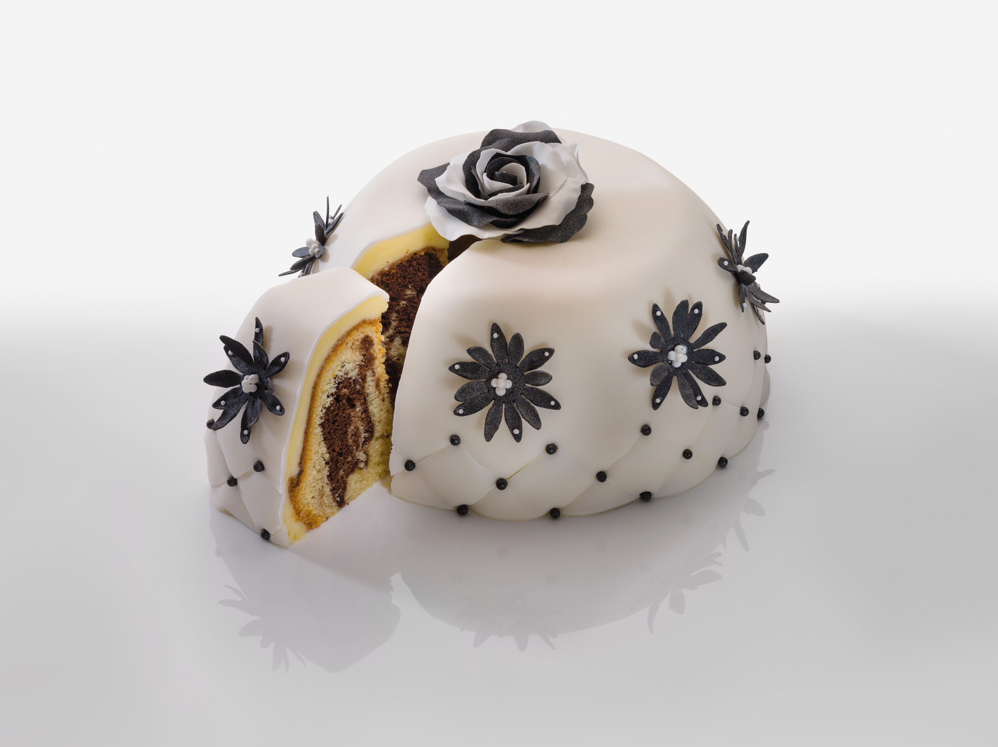 Weißer Kuchen mit einem herausgeschnittenen Stück. Es hat schwarze Blumendekorationen und eine Rose.