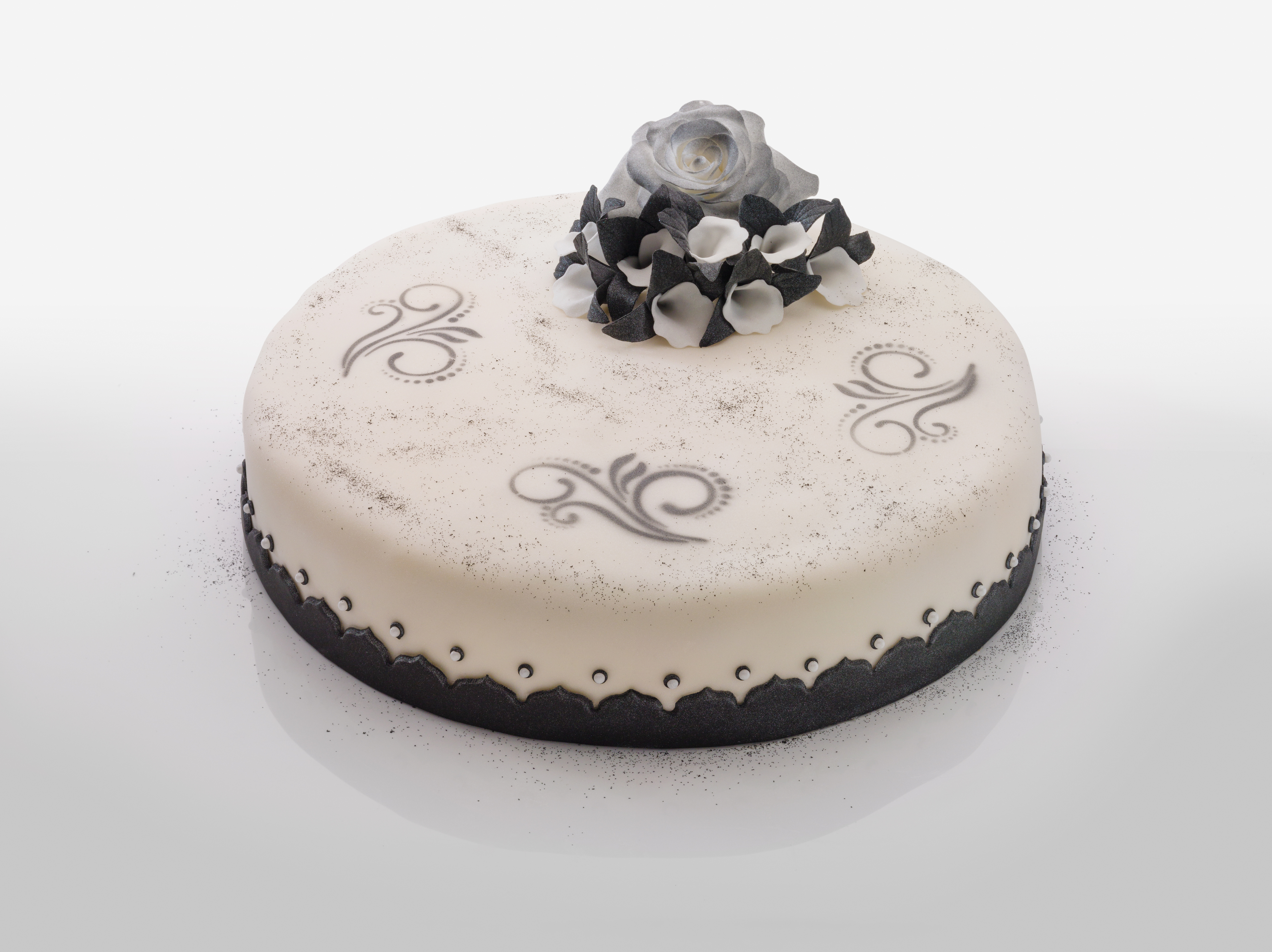 Runder Kuchen mit weißem Zuckerguss, grauen Verzierungen und Blumenspitze.