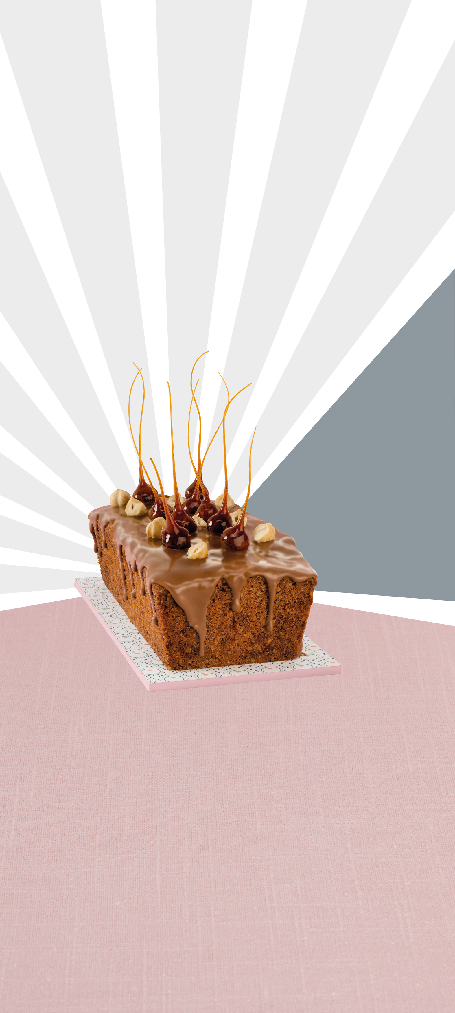 Kuchen mit Zuckerguss, Haselnüssen und Karamellstangen. Rosa und grauer Hintergrund.