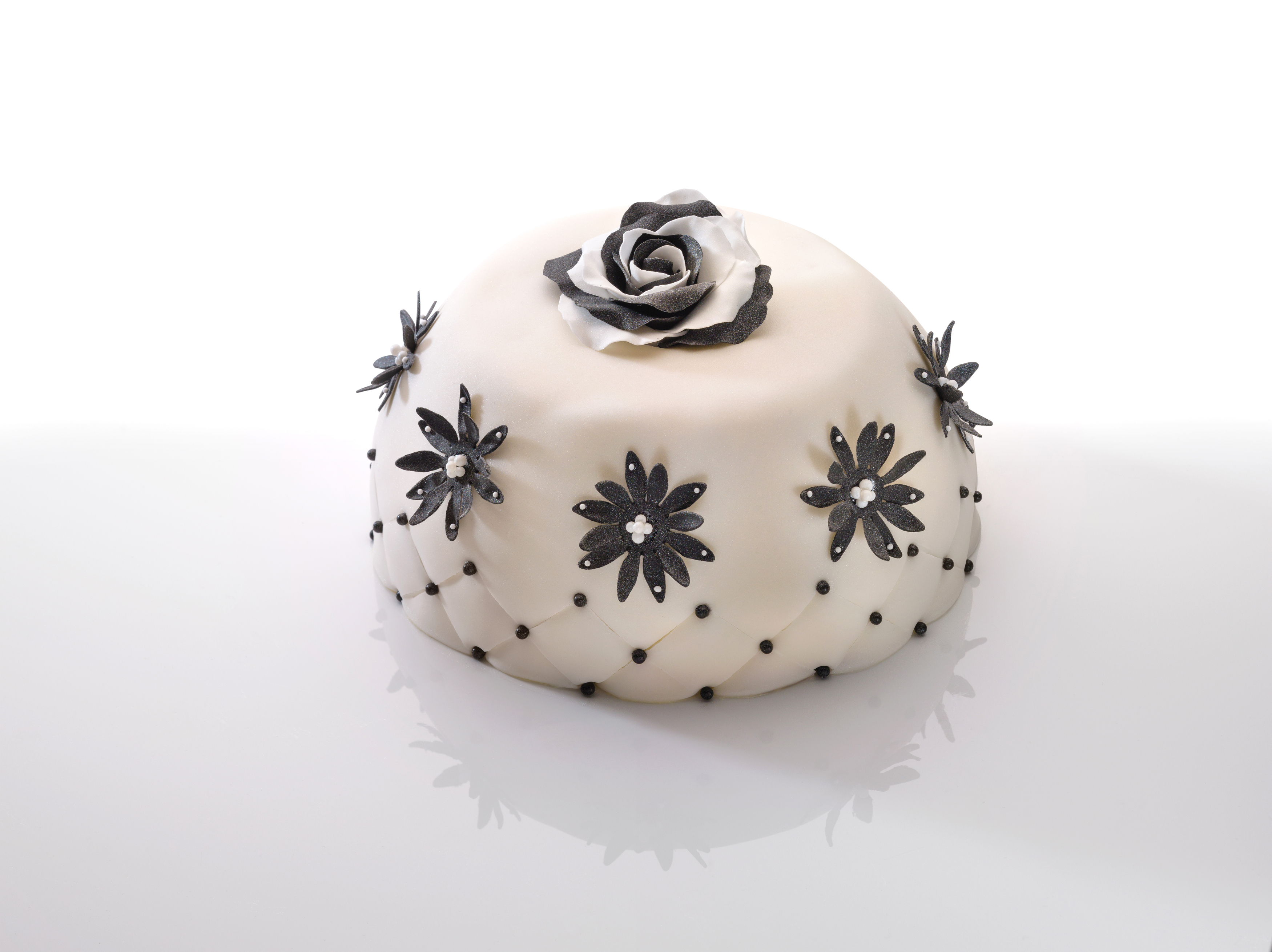 Runder weißer Kuchen mit schwarzen und grauen Blumendekorationen und Steppmuster auf weißer Oberfläche.