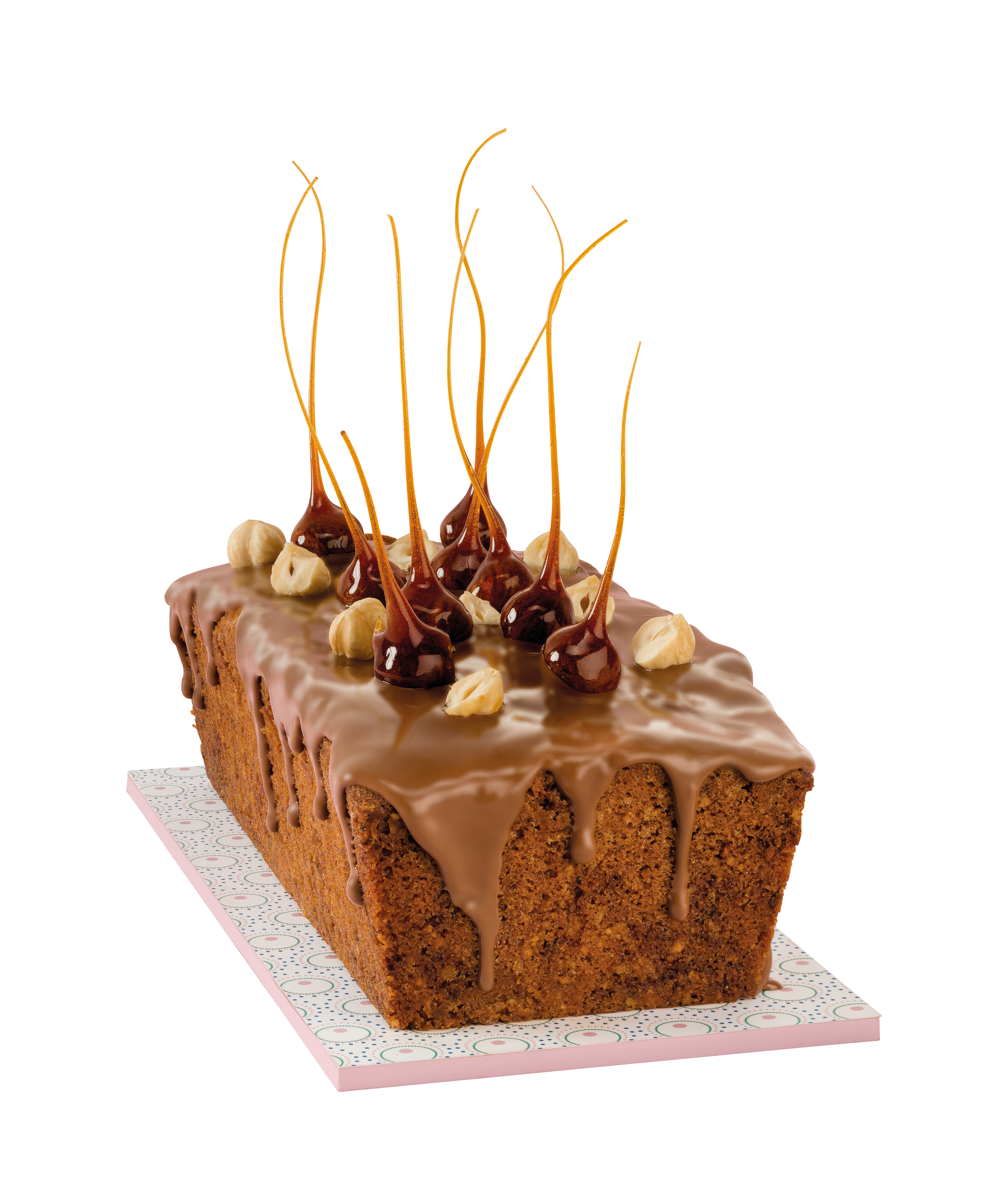 Ein Kuchen mit Karamellverzierungen und Nüssen auf rosa Oberfläche.