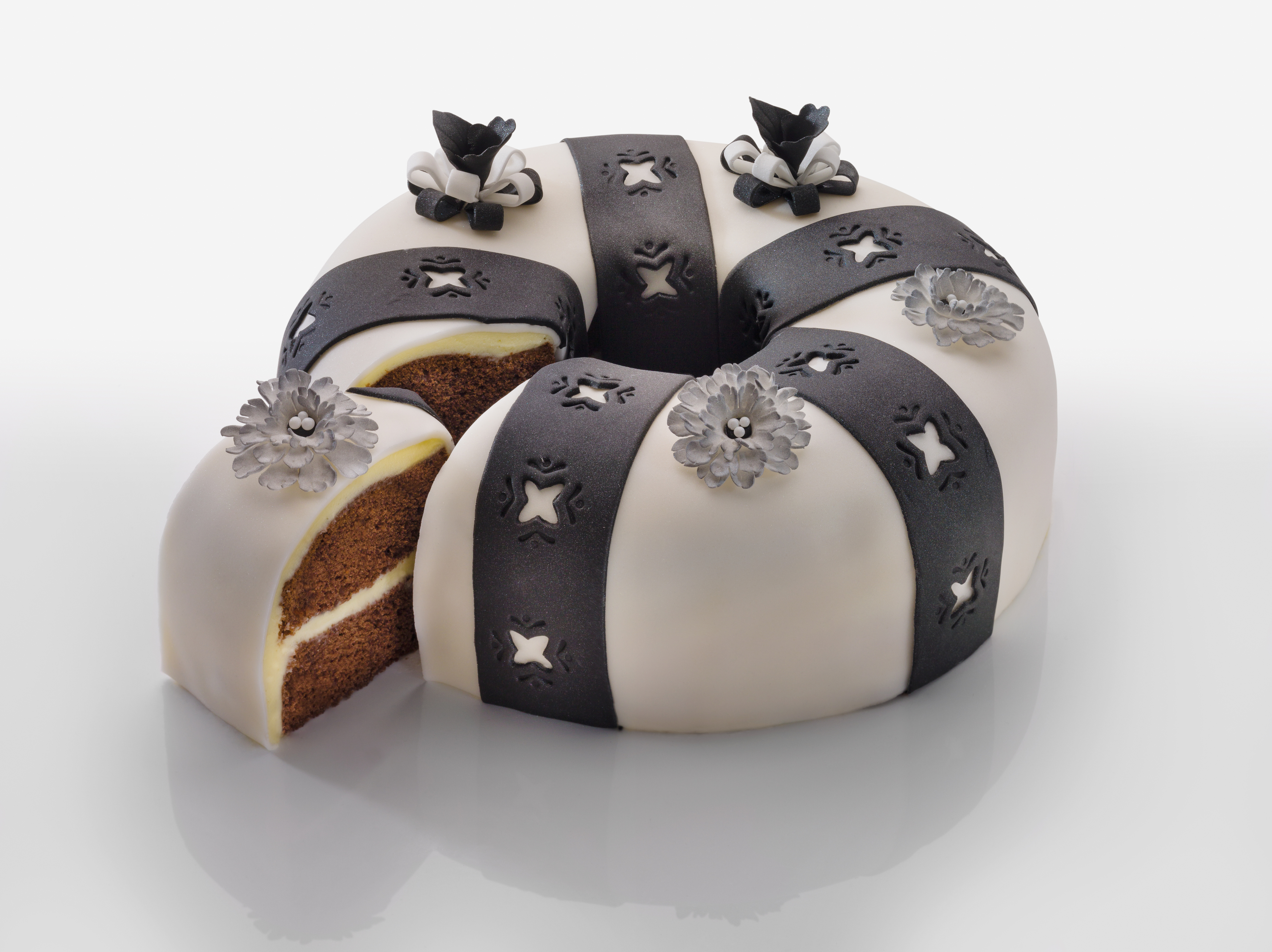 Eine weiße Torte mit schwarzen Verzierungen. Ein Stück ist geschnitten. Blumen oben drauf.