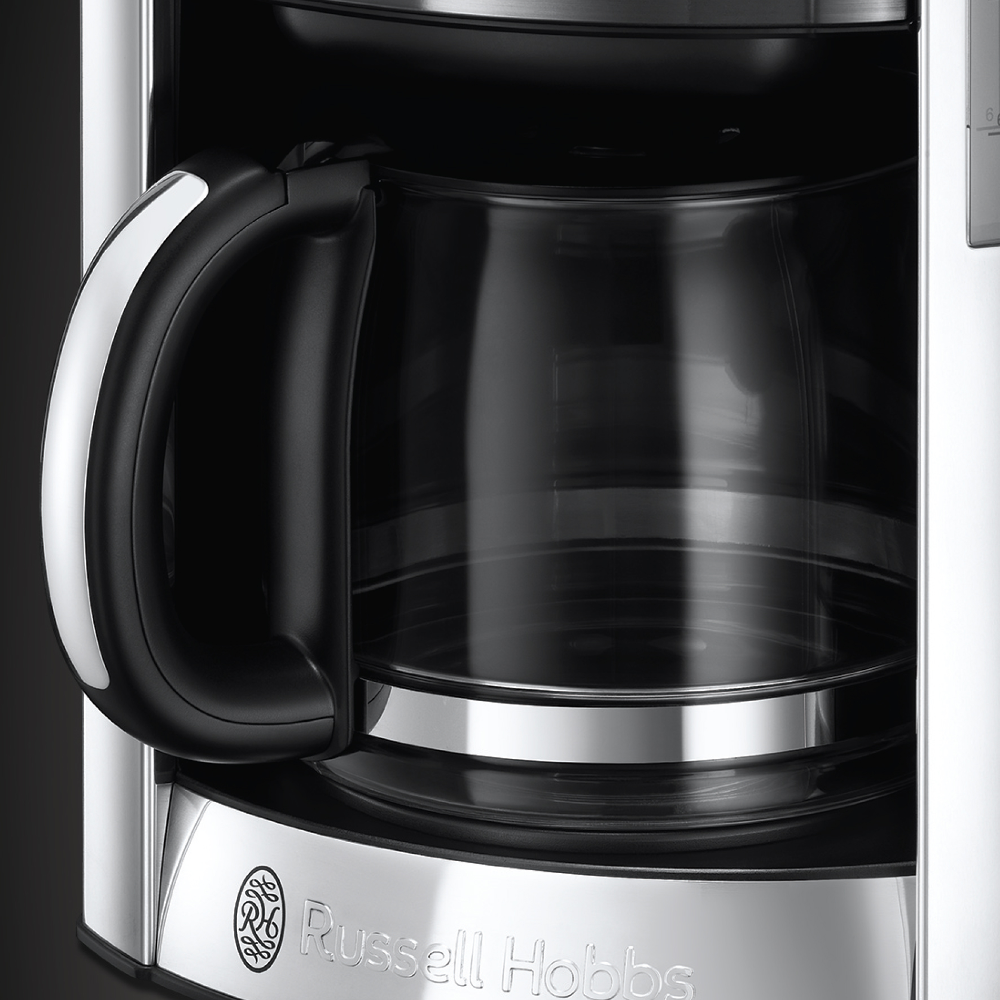 Close-up of a coffee maker. Black handle, glass carafe, and Russell Hobbs logo.