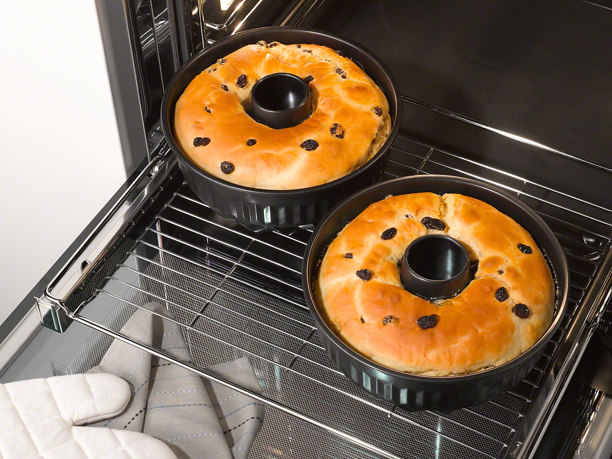 Zwei runde Kuchen mit Rosinen in einer schwarzen Backform im Ofen.