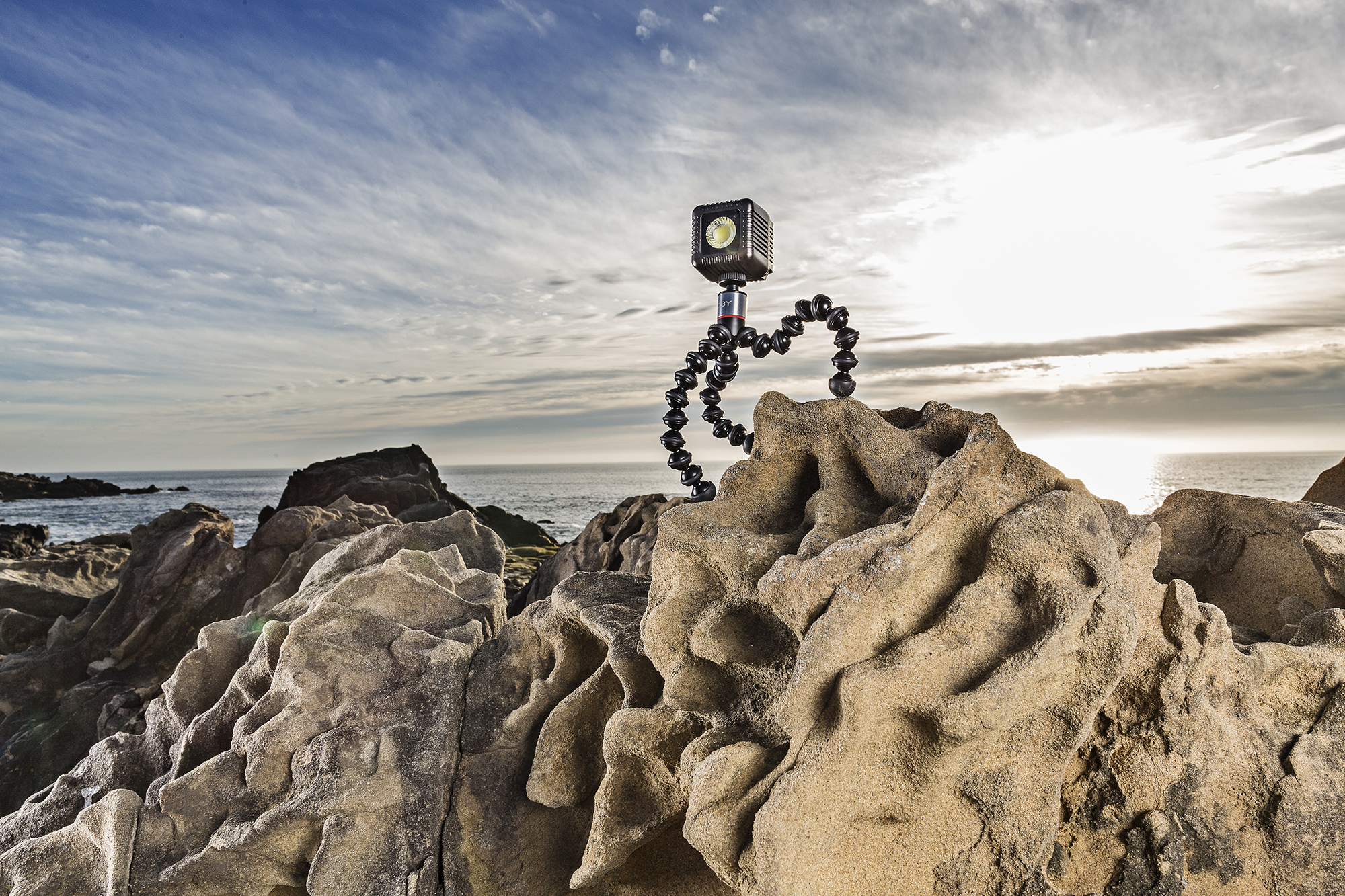 A small light on a flexible tripod on a rock next to the ocean at sunset.