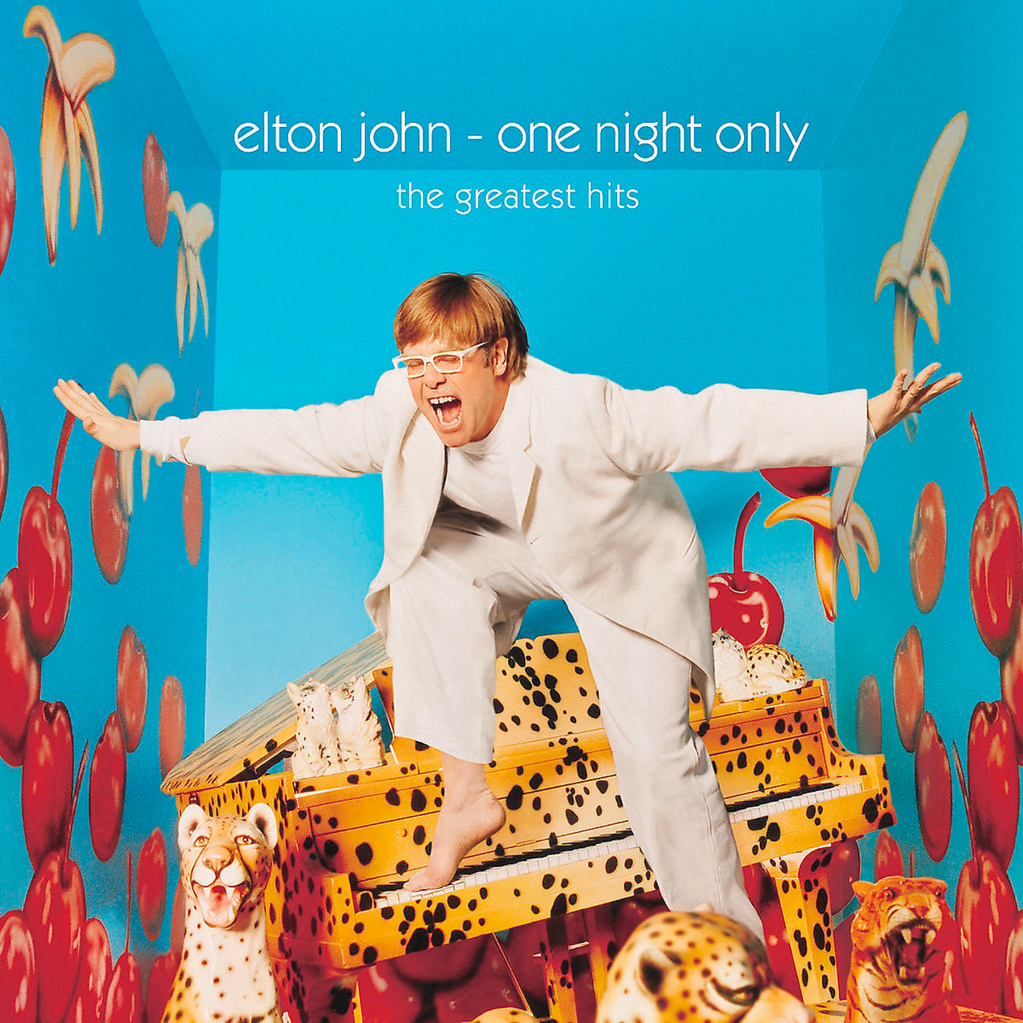 Elton John auf einem Klavier mit Leopardenmuster. Er trägt Weiß und hat die Arme oben.
