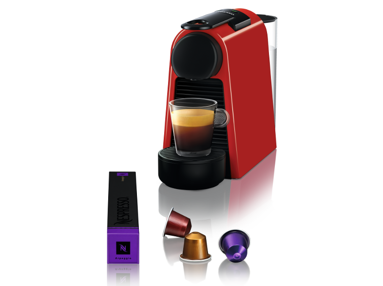 Piros Nespresso gép egy pohár kávéval és kapszulákkal fekete háttér előtt.