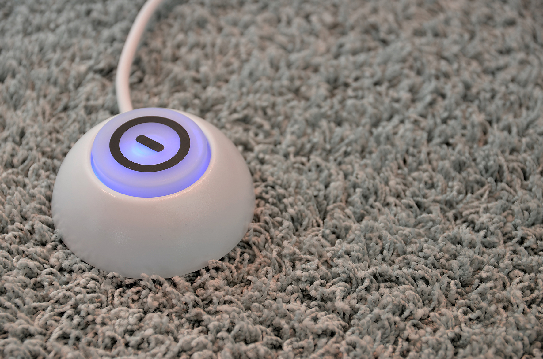 Weißes kreisförmiges Gerät mit Knopf auf grauem Teppich. Blaues Licht.