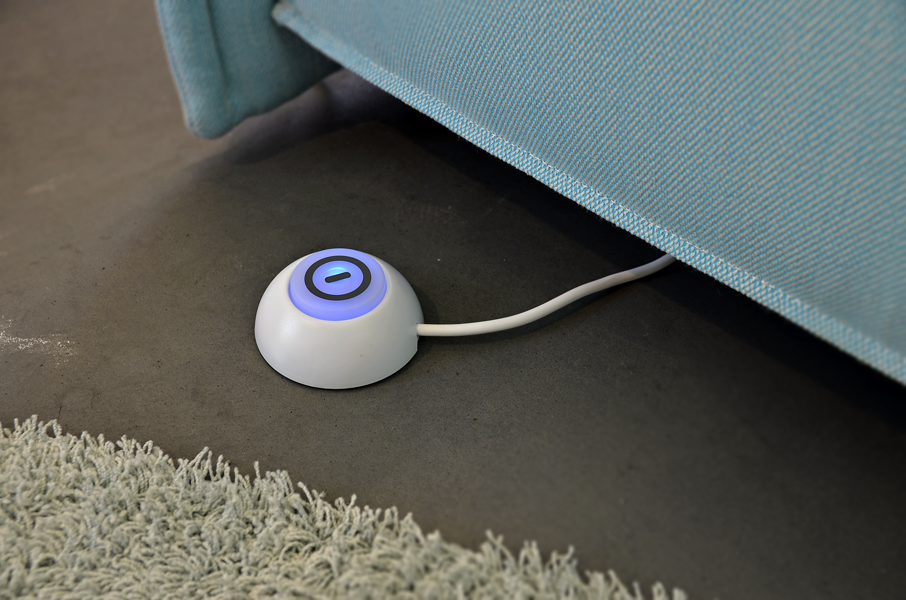 Eine weiße Fernbedienung mit blauem Licht auf einem Boden neben einem blauen Sofa.
