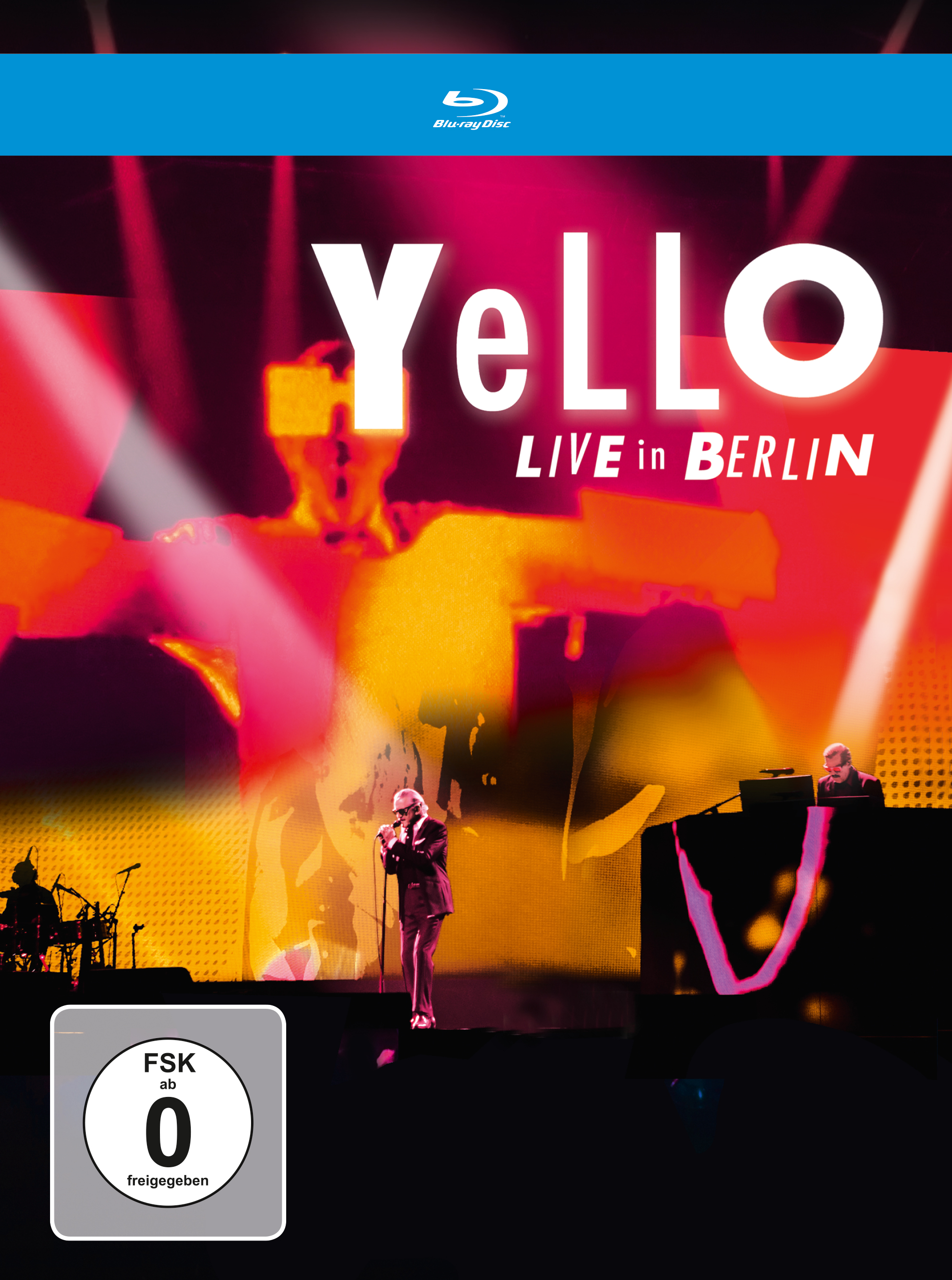 Yello Live in Berlin Blu-Ray Cover: Ein Mann singt auf der Bühne mit Hintergrundlichtern und Bandmitgliedern.