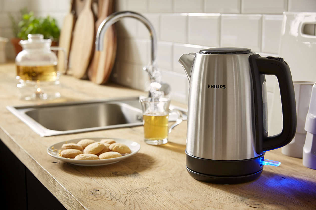 Stainless steel kettle with black handle and blue light, water running from the faucet, cookies on a plate.
